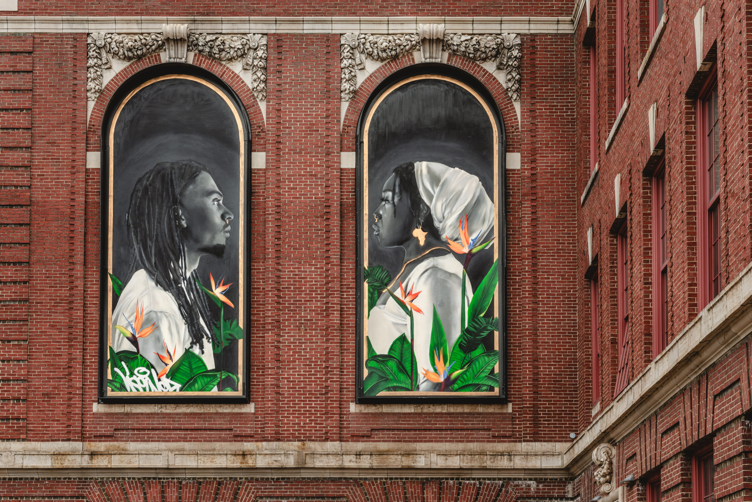 Two arched paintings of people facing one another installed in the exterior arched brickwork of MassArt's South building