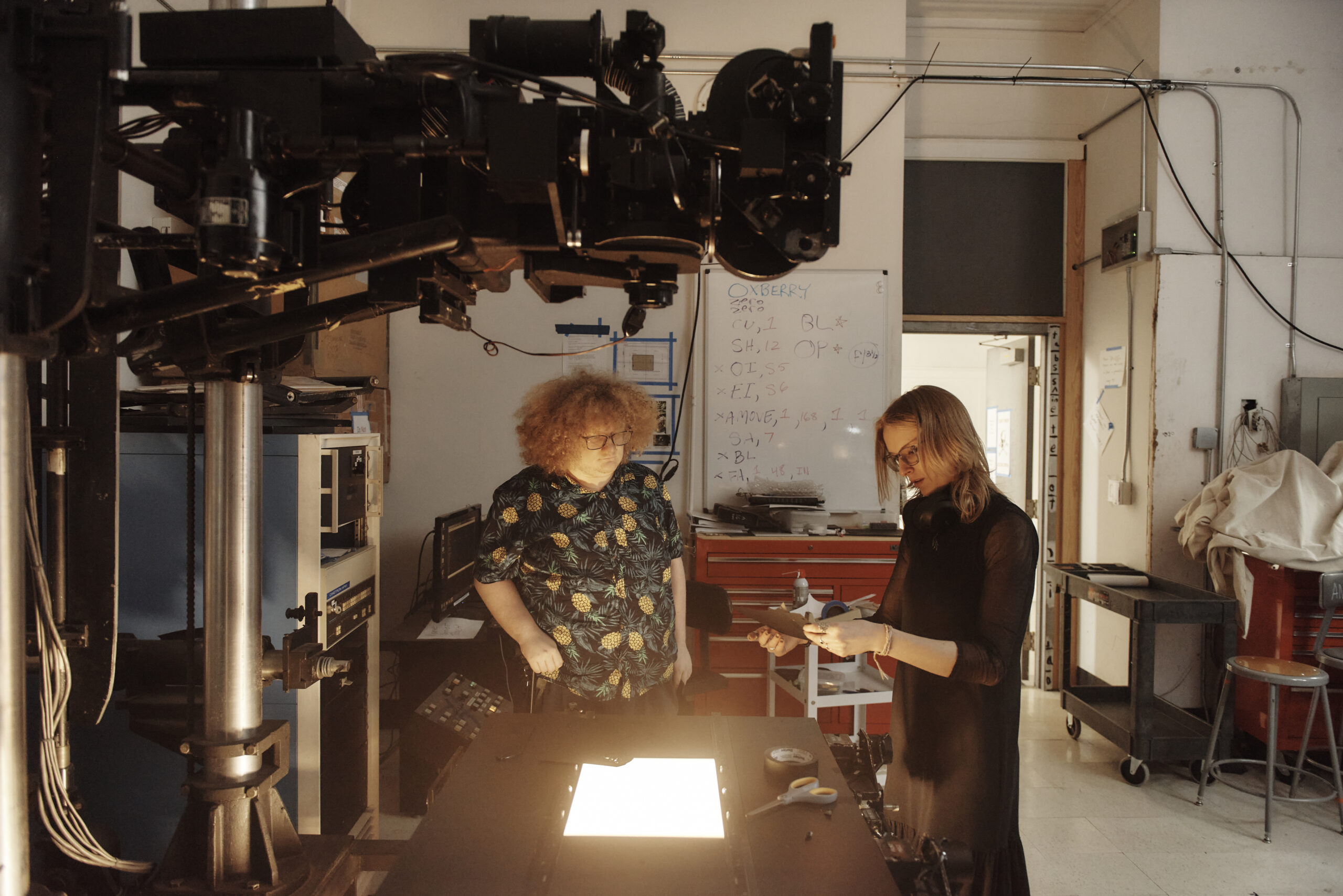 A light table glowing in the center of the frame with two people working around it and animation equipment above the table.