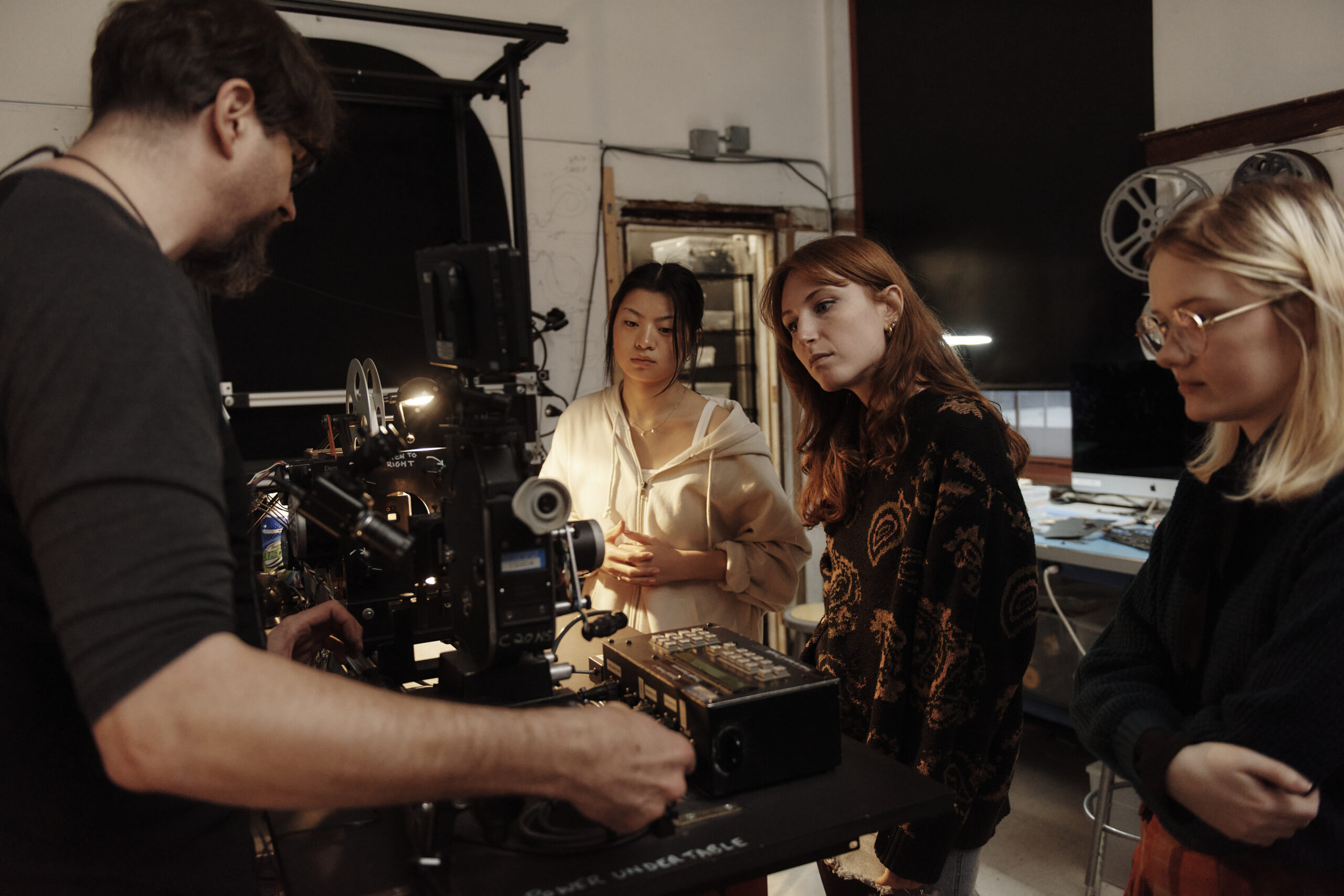 Two students watch as a professor shows how to use animation film equipment