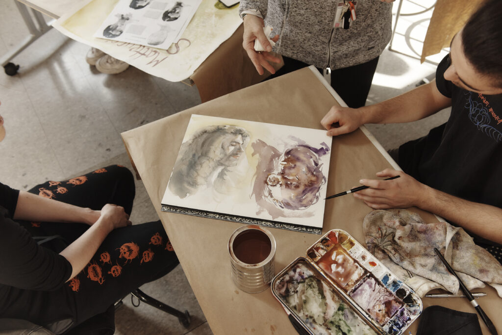 Looking down at a watercolor painting on a table with people around the table.