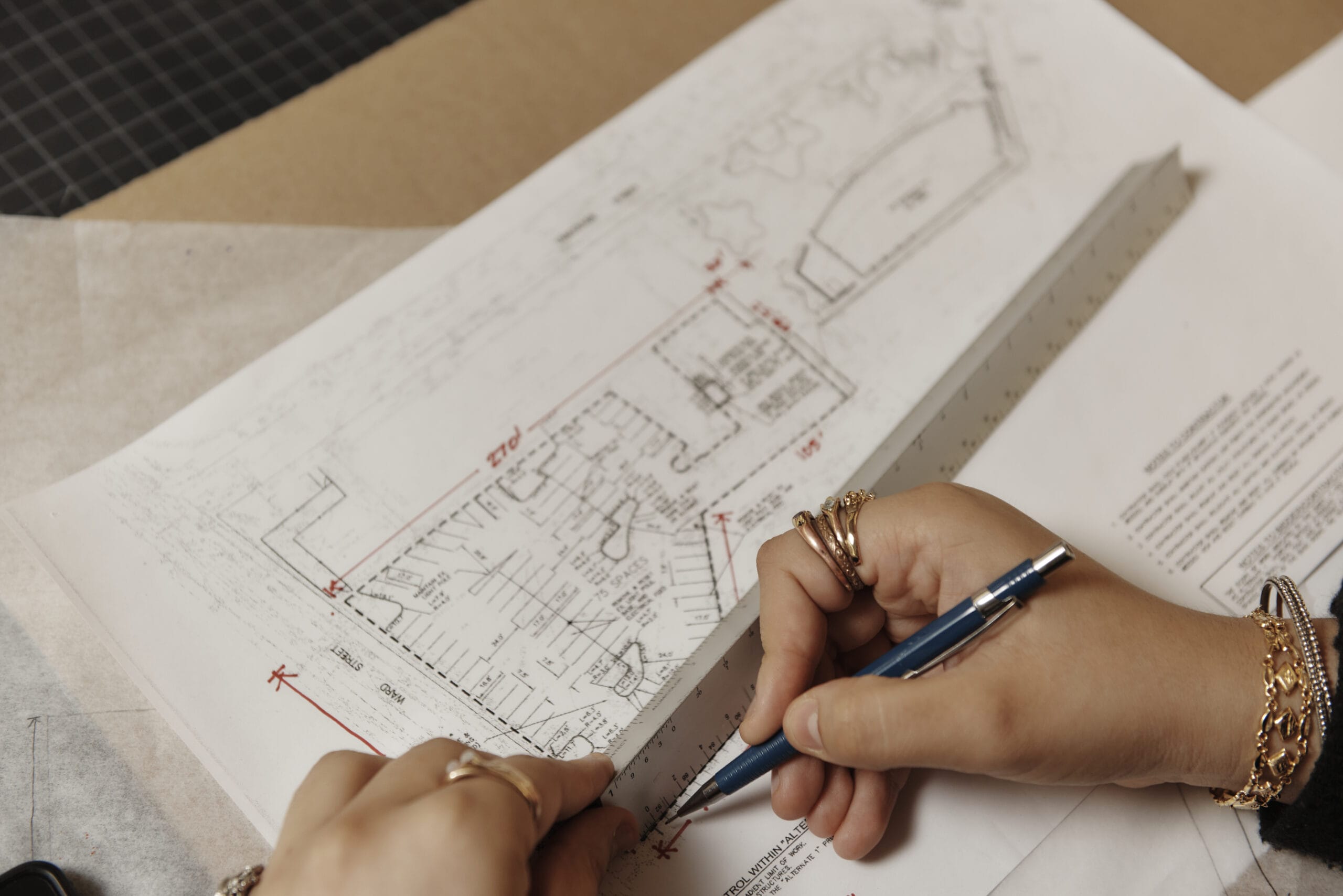 Close up of a hand and ruler drawing a straight line on architectural plans.