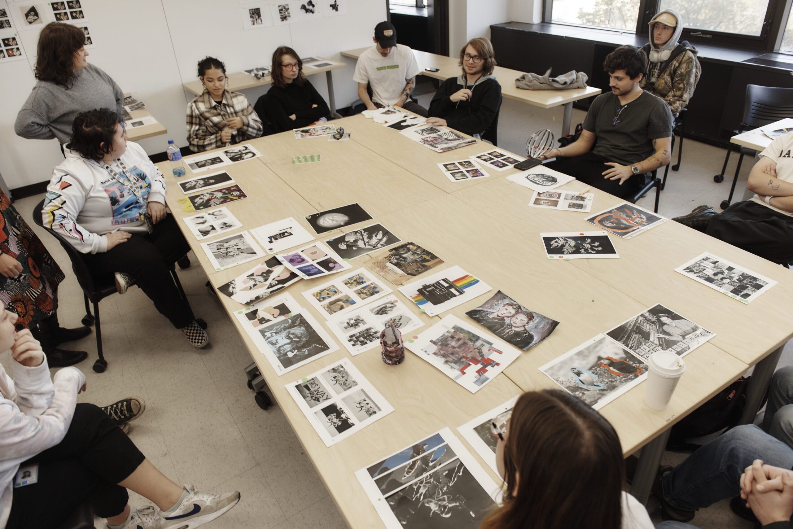 Students all sitting around a large table tiled with design work.