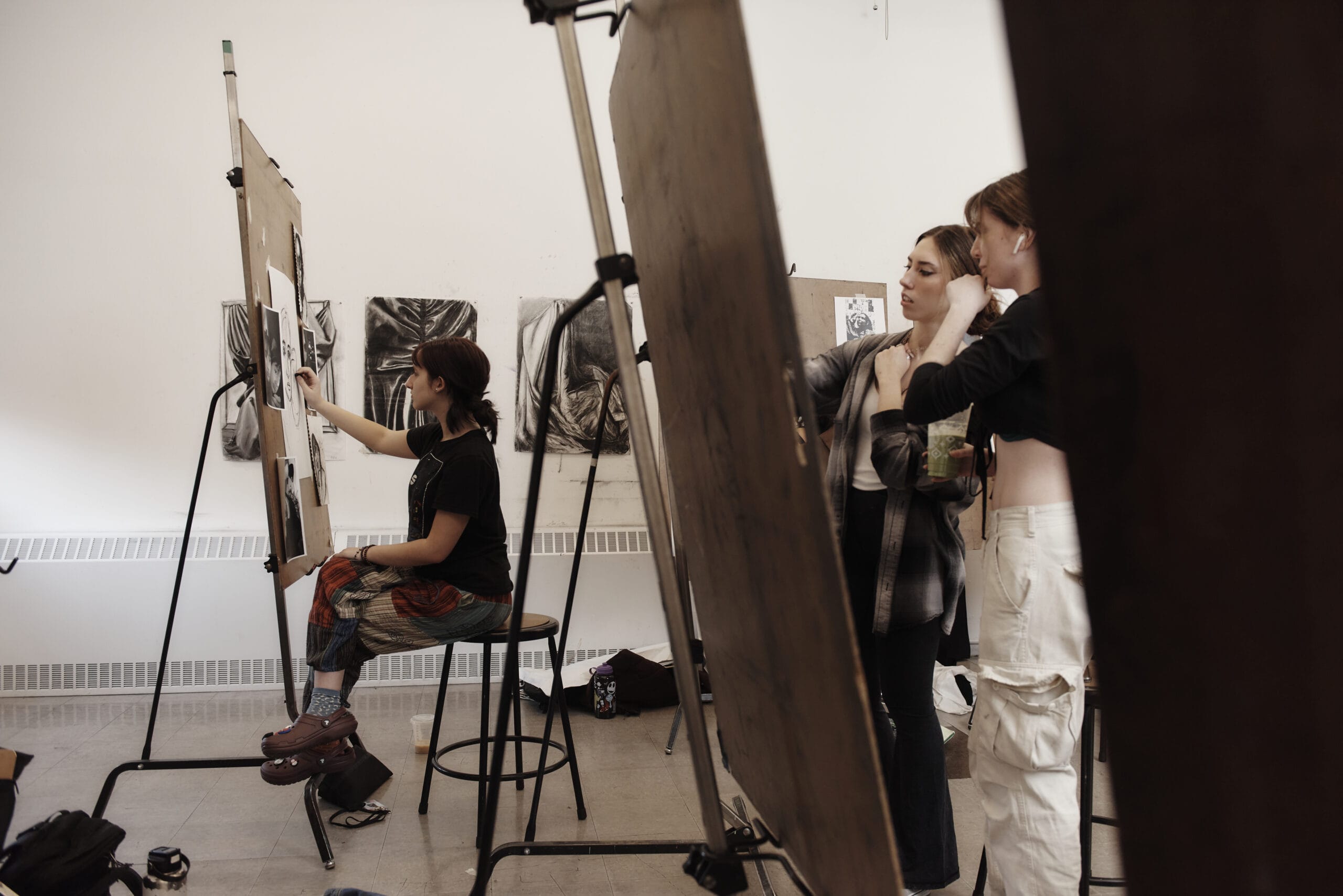 Students stand at easels drawing with charcoal.