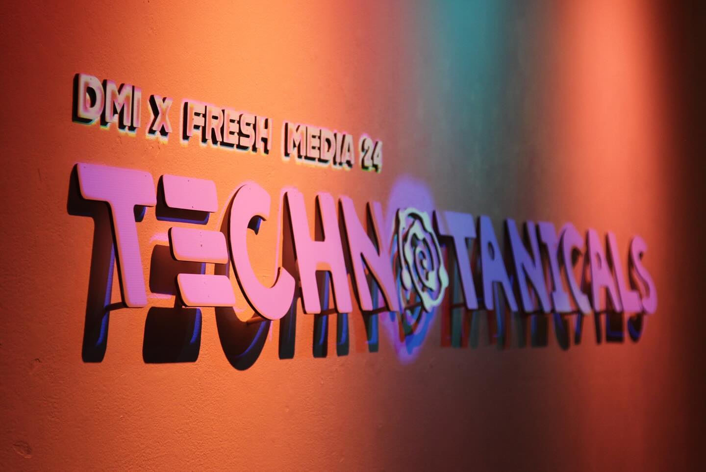 Sign on an orange wall that says DMI x FreshMedia Technotanicals
