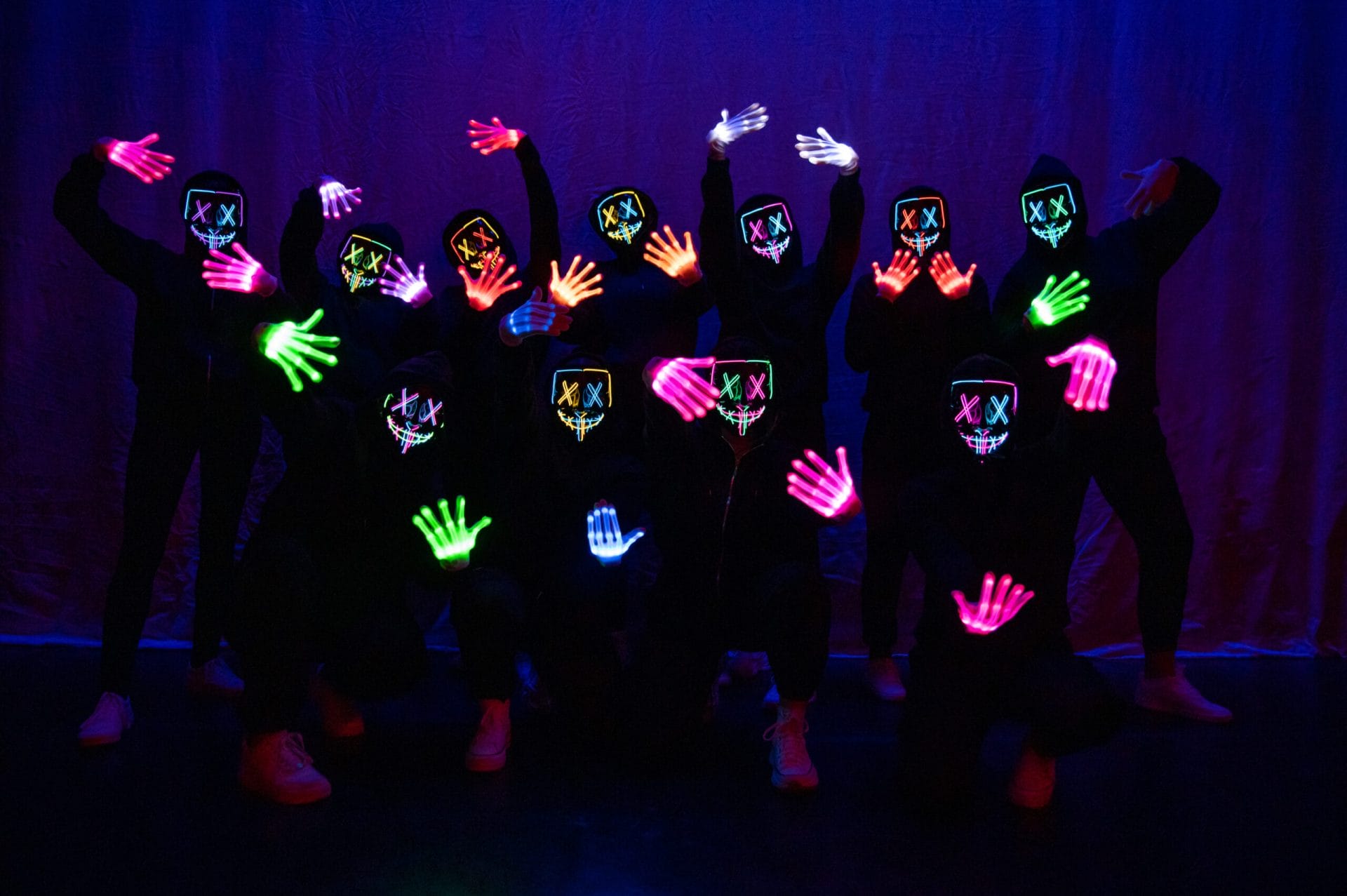 Dancers posing on a dark stage in glow-in the dark masks and gloves