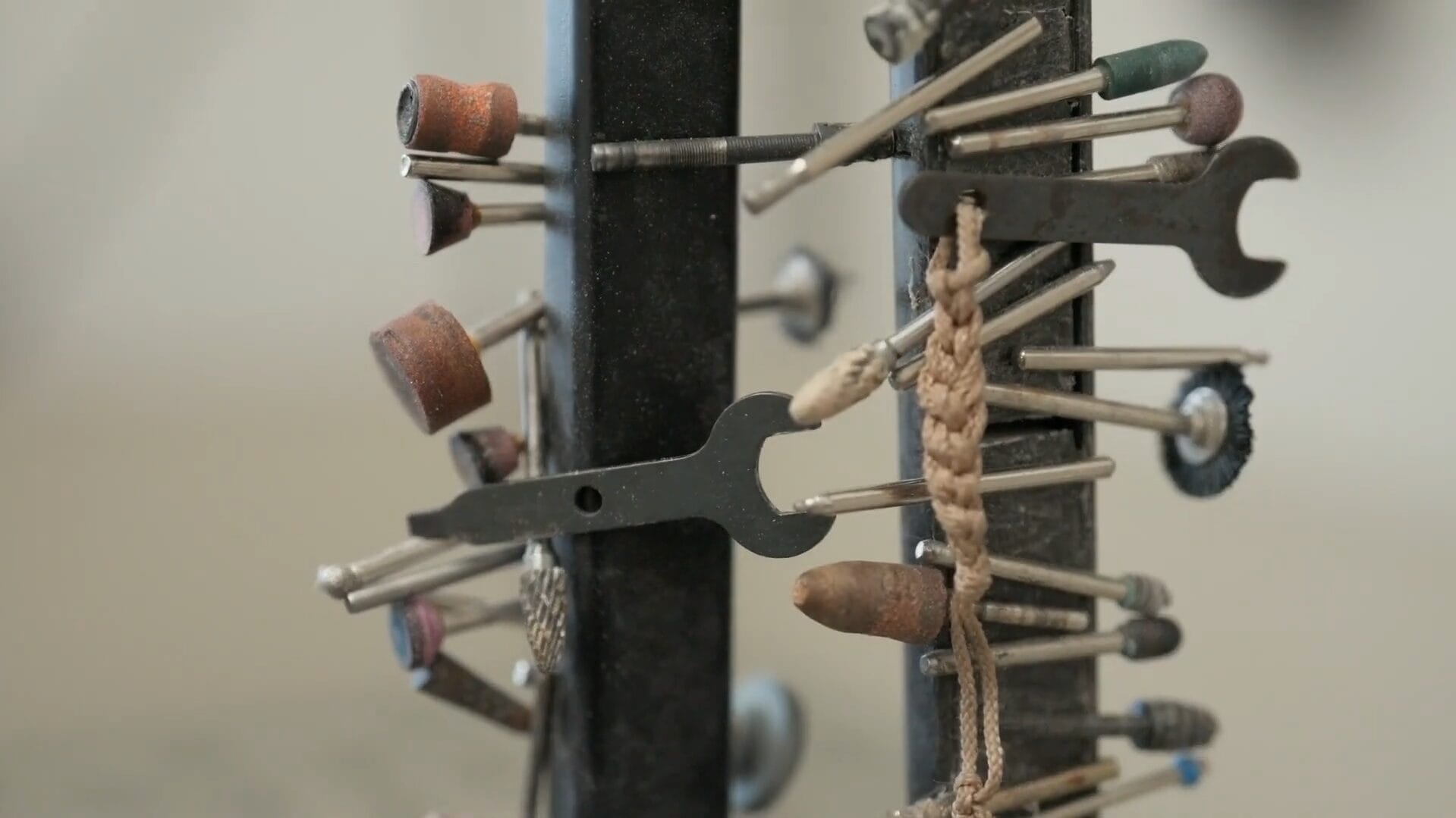 A close-up of a rotating tool stand, often found in Communication Design studios, holding various small grinding and polishing attachments, wrenches, and a piece of knotted string for jewelry making or fine metalwork.