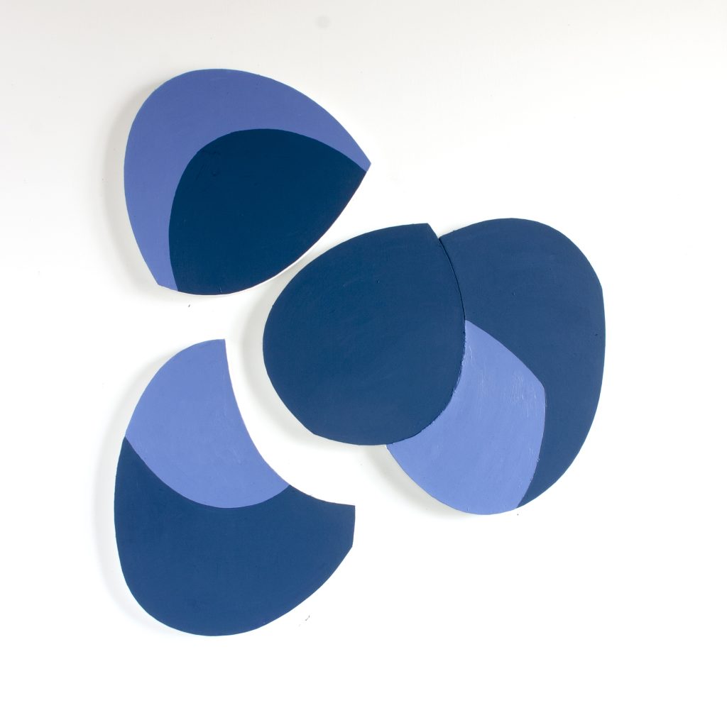 Abstract artwork with three overlapping, irregularly shaped pieces in shades of blue and purple, set against a white background. The pieces have smooth edges, resembling a modern, minimalist style.