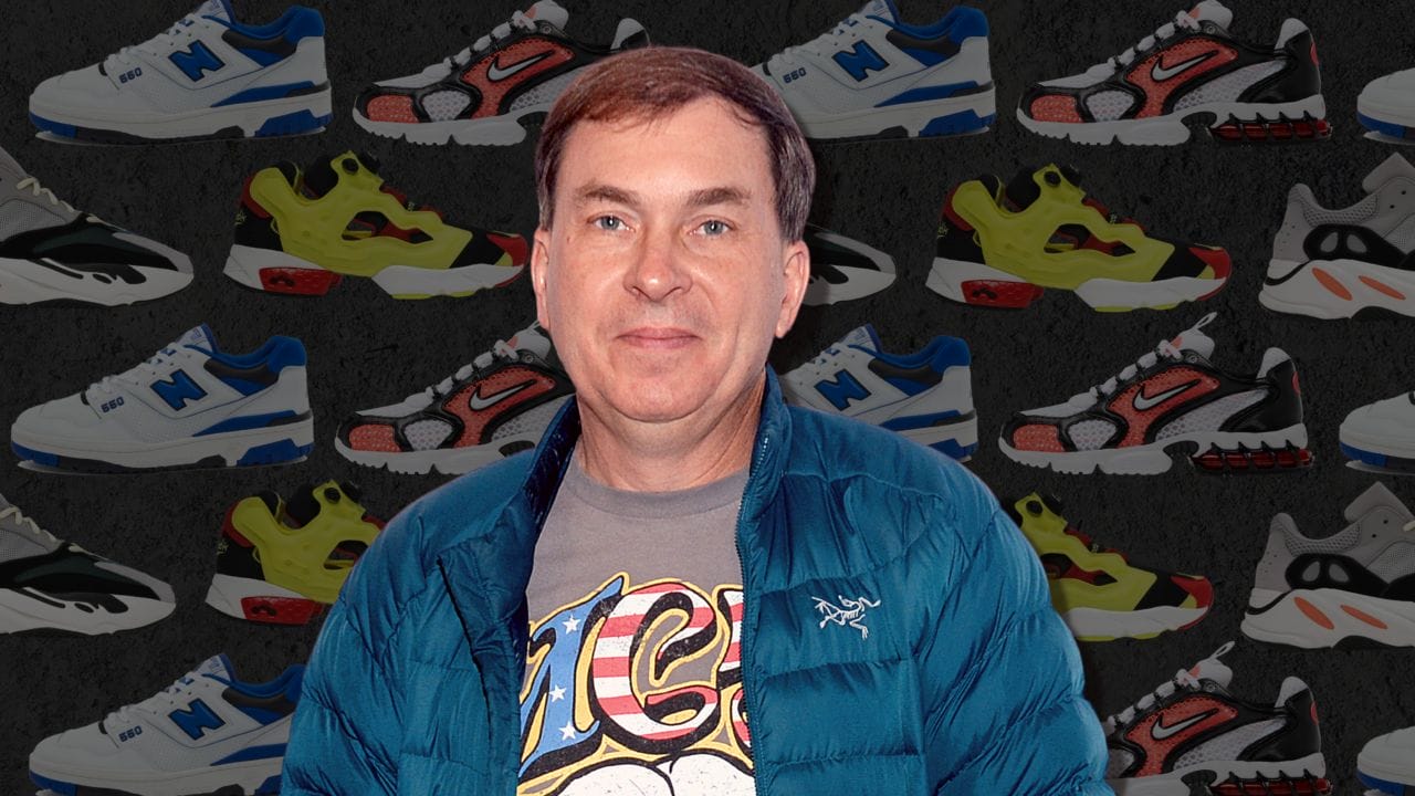 Steven Smith, in a blue jacket, stands against a backdrop of colorful sneakers. Sporting a graphic t-shirt, he beams at the camera.
