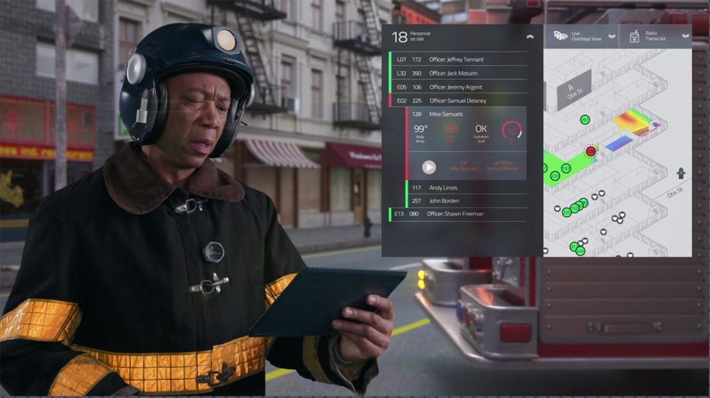 A firefighter in a black helmet and coat studies a tablet, utilizing Fire Command technology to access a digital display with building floor plans, occupancy details, and emergency data. A fire truck and buildings serve as the backdrop for this critical moment in emergency response.