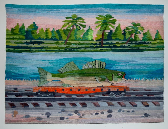 A vibrant tapestry from the Franklin Gallery by Suzanne Pretty portrays a large fish resting on a flat car of a train, journeying along railroad tracks. In the background, palm trees sway beside a river under a sunset sky awash with shades of pink and blue.