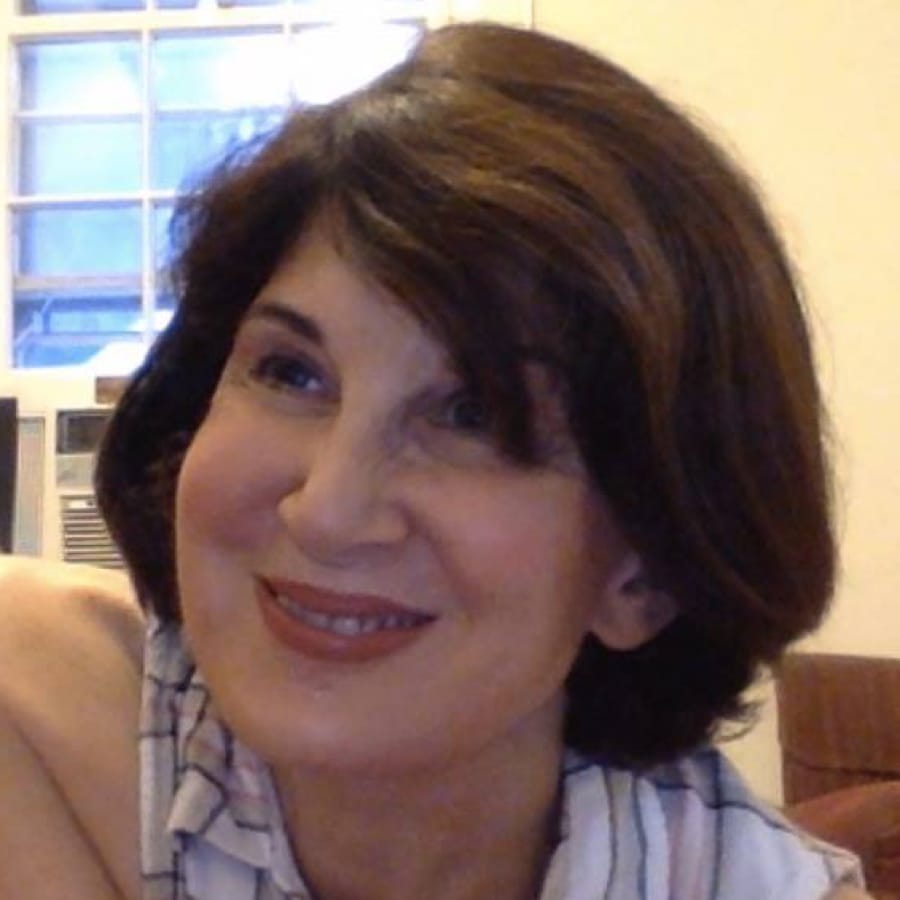 Smiling woman with short, brown hair in a striped shirt. Shes indoors near a window and air conditioner.