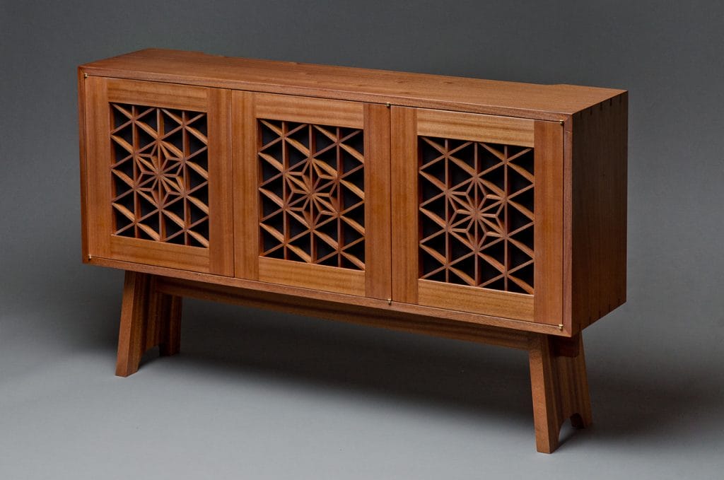 A modern designed wooden media cabinet with intricate designs in the doors.