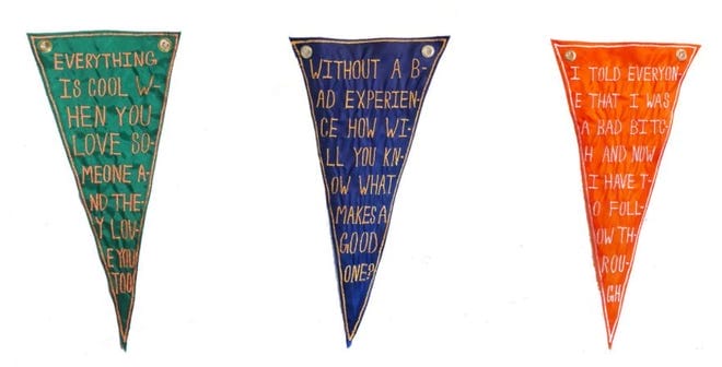 Three triangular banners with handwritten text celebrate the charm of public art installations. Left: Green with Everything is cool when you love someone and the way you love you too. Center: Blue with Without a bad experience, how will you know what makes a good one? Right: Orange reflecting on lifes lessons.