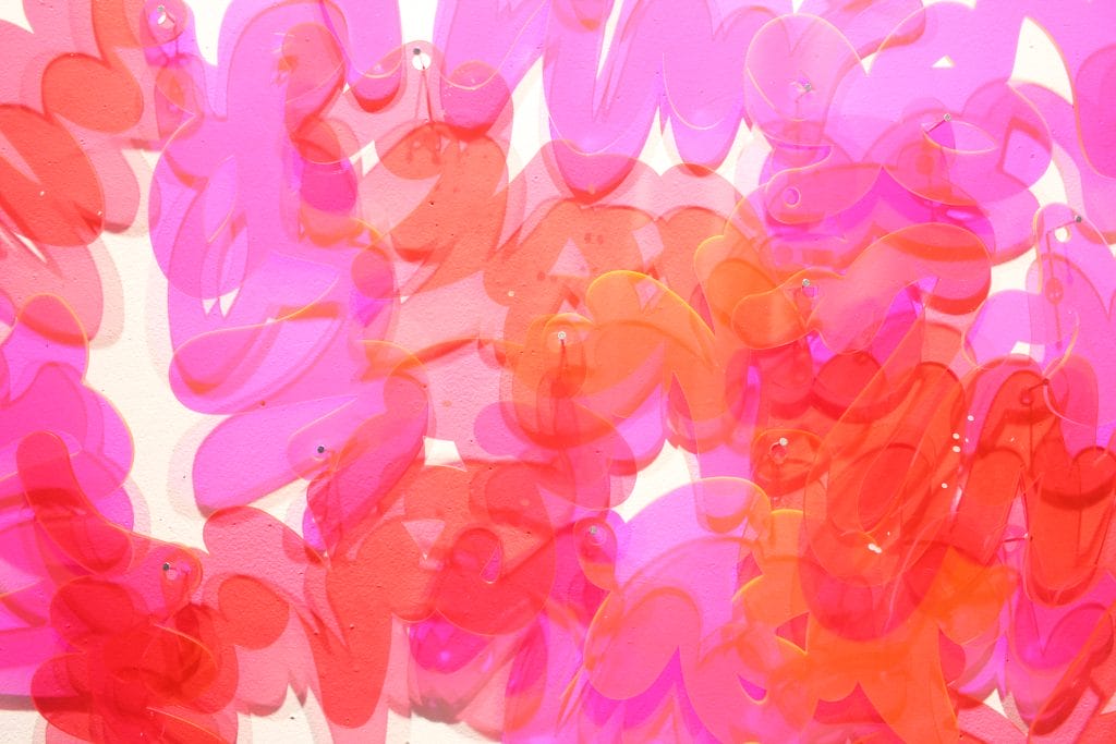 Abstract artwork featuring overlapping, translucent brushstrokes in pink, red, and orange hues against a light background. The detailed shapes evoke a sense of dancing movement and depth.