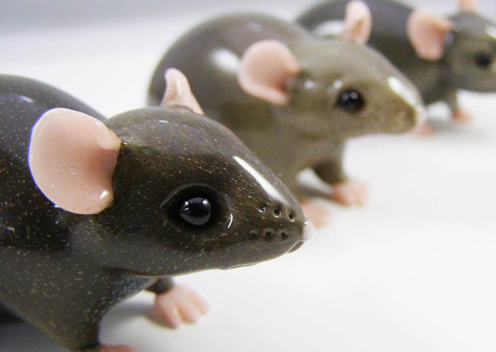 Close-up of ceramic mice figurines lined up diagonally. They have glossy dark bodies, pink ears, and small eyes. The focus is on the first figurine, with a blurred view of the others in the background.
