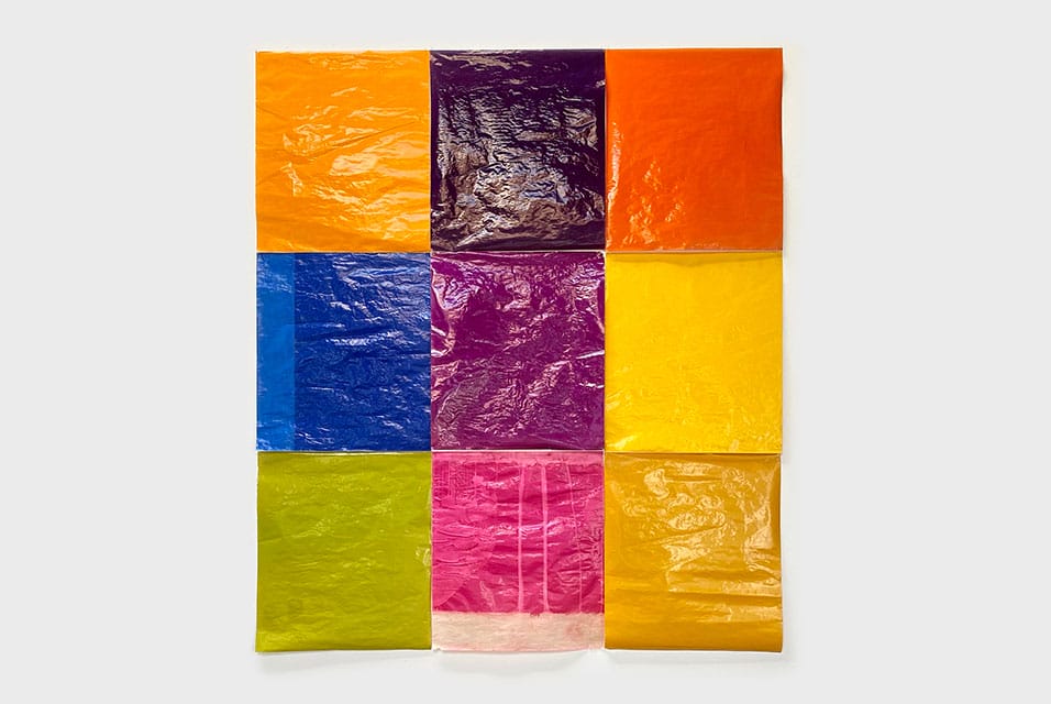 A vibrant grid of nine colorful crinkled sheets adorns the white backdrop, resembling a Jack Pierson exhibition at Regen Projects. The colors—orange, dark purple, bright orange, blue, purple, yellow, lime green, pink, and orange-yellow—flow from top left to bottom right with artistic flair.