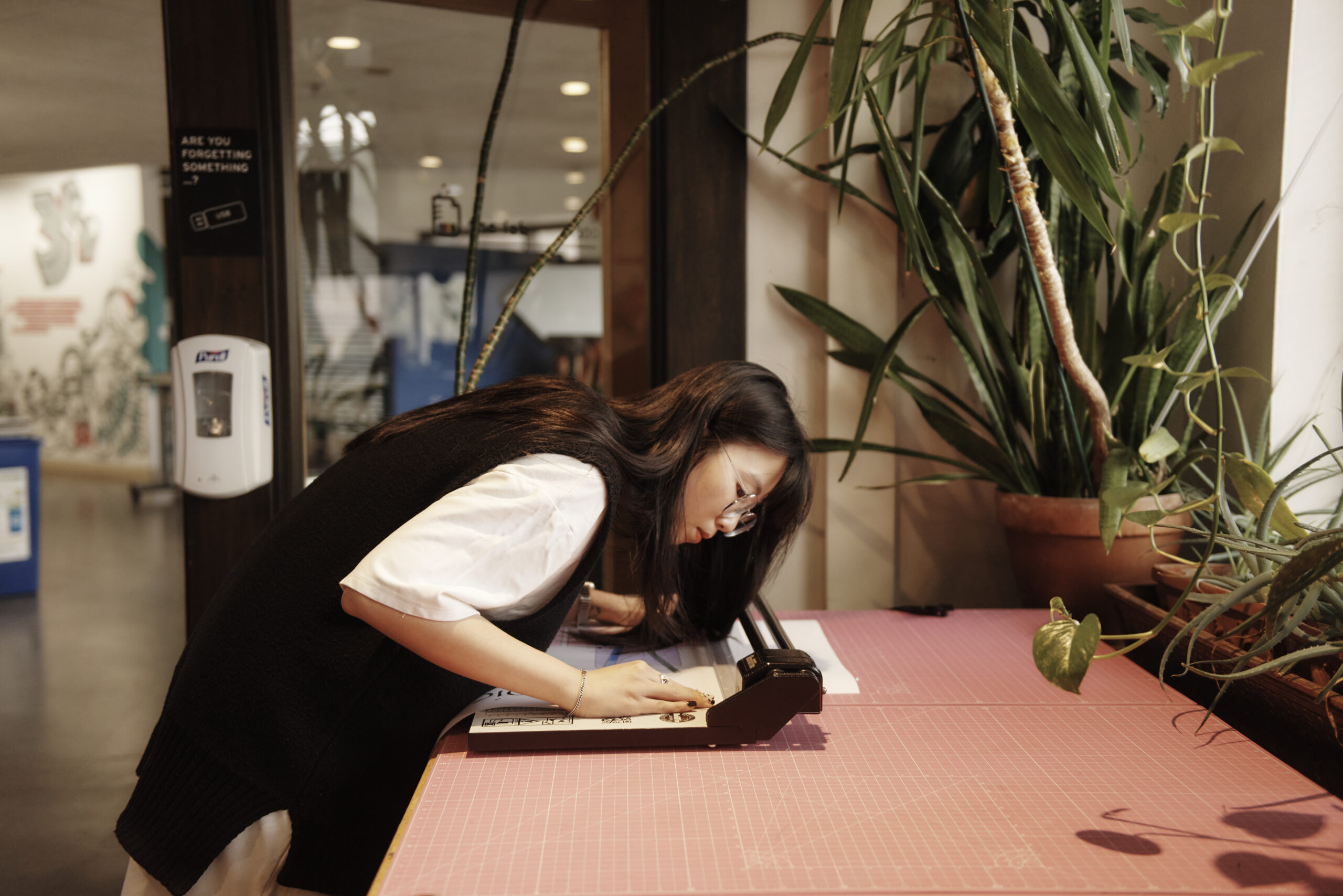 A woman leans over to use a paper cutter.