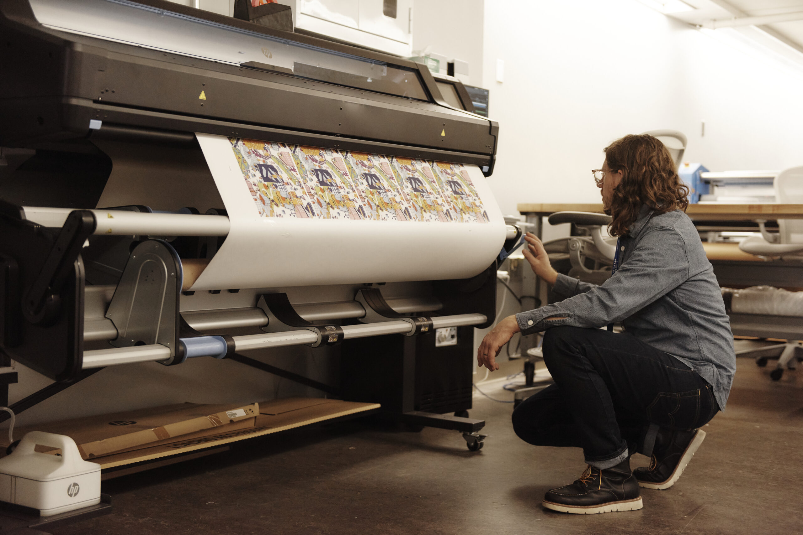 A staff person squatting in front of a wide roll printer in the lab.