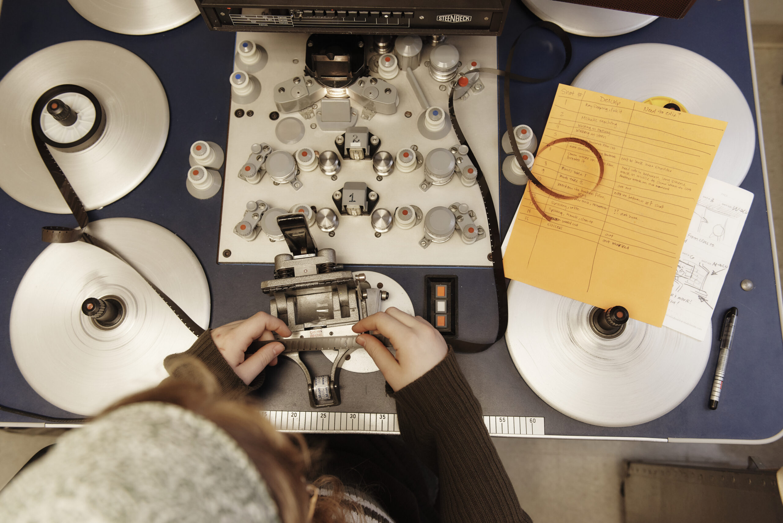 A person sits at a table with film winding spools, looking at a filmstrip.