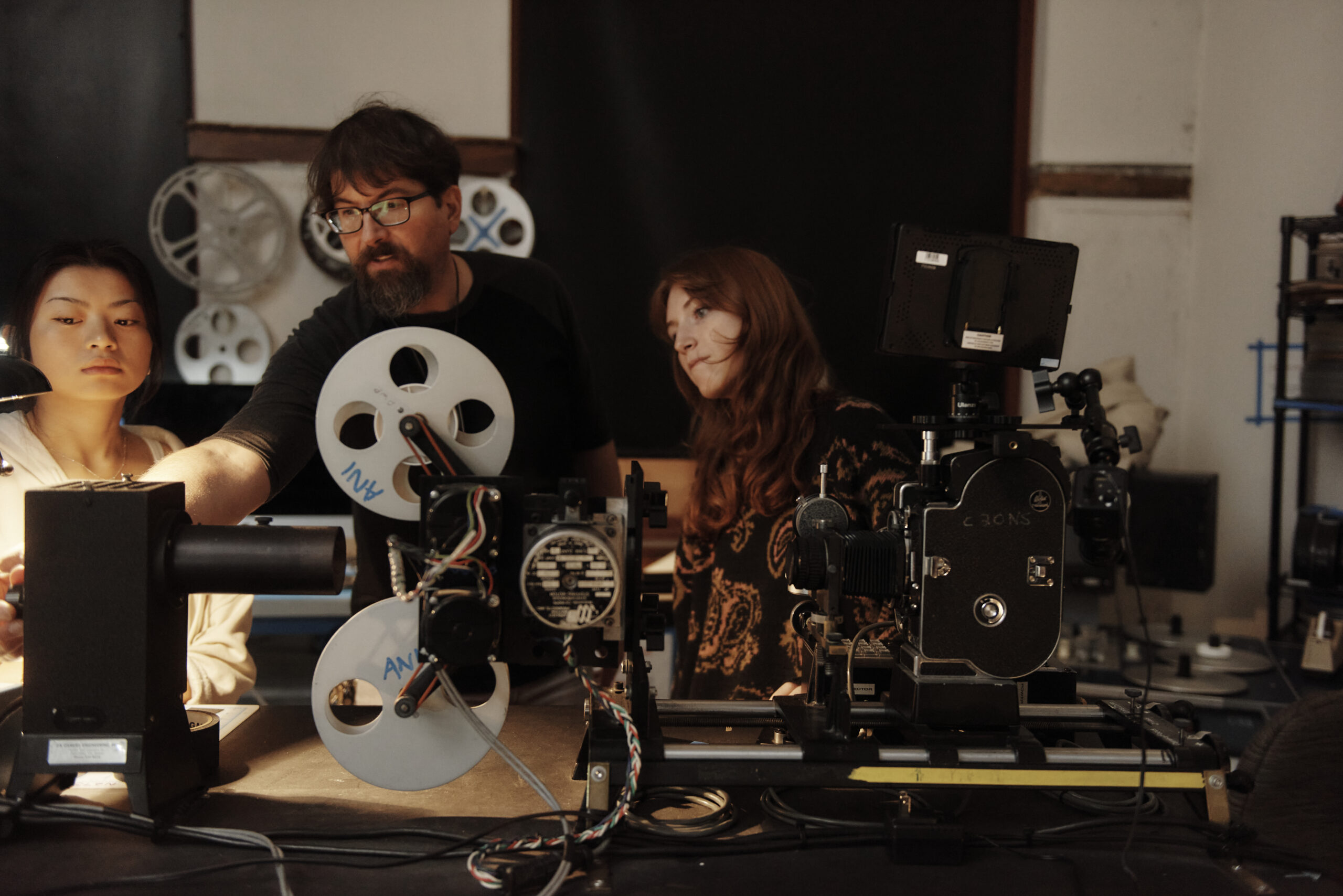 A professor shows two students how to use a film projector
