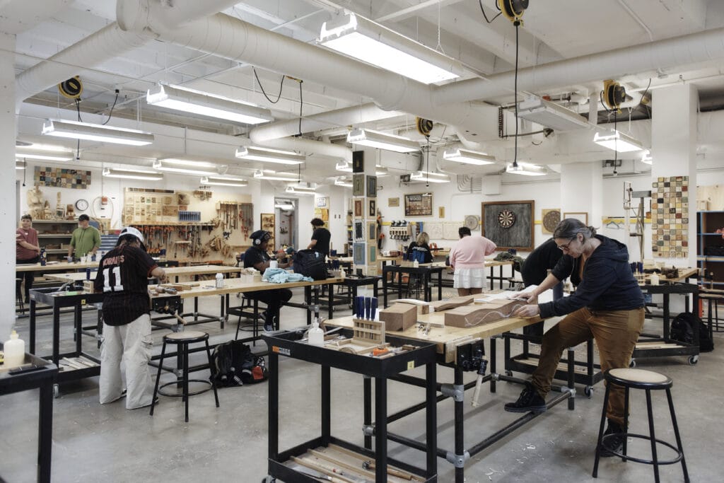 Many students standing at tables working in a woodshop.