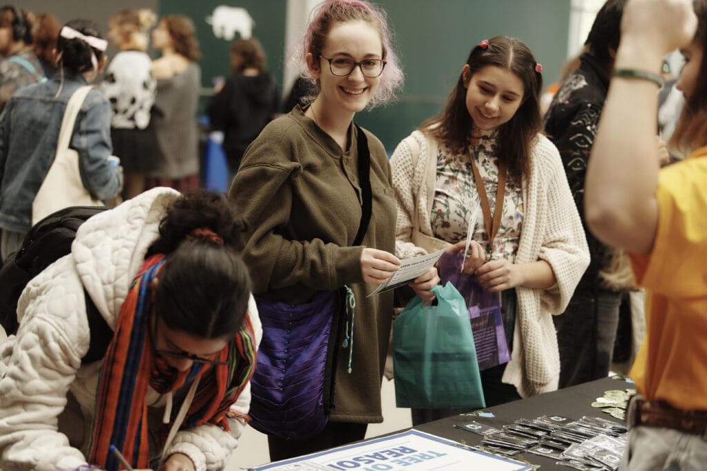 A student smiles at the camera as she stands at a Community Health and Wellness fair in MassArt's Design and Media Center