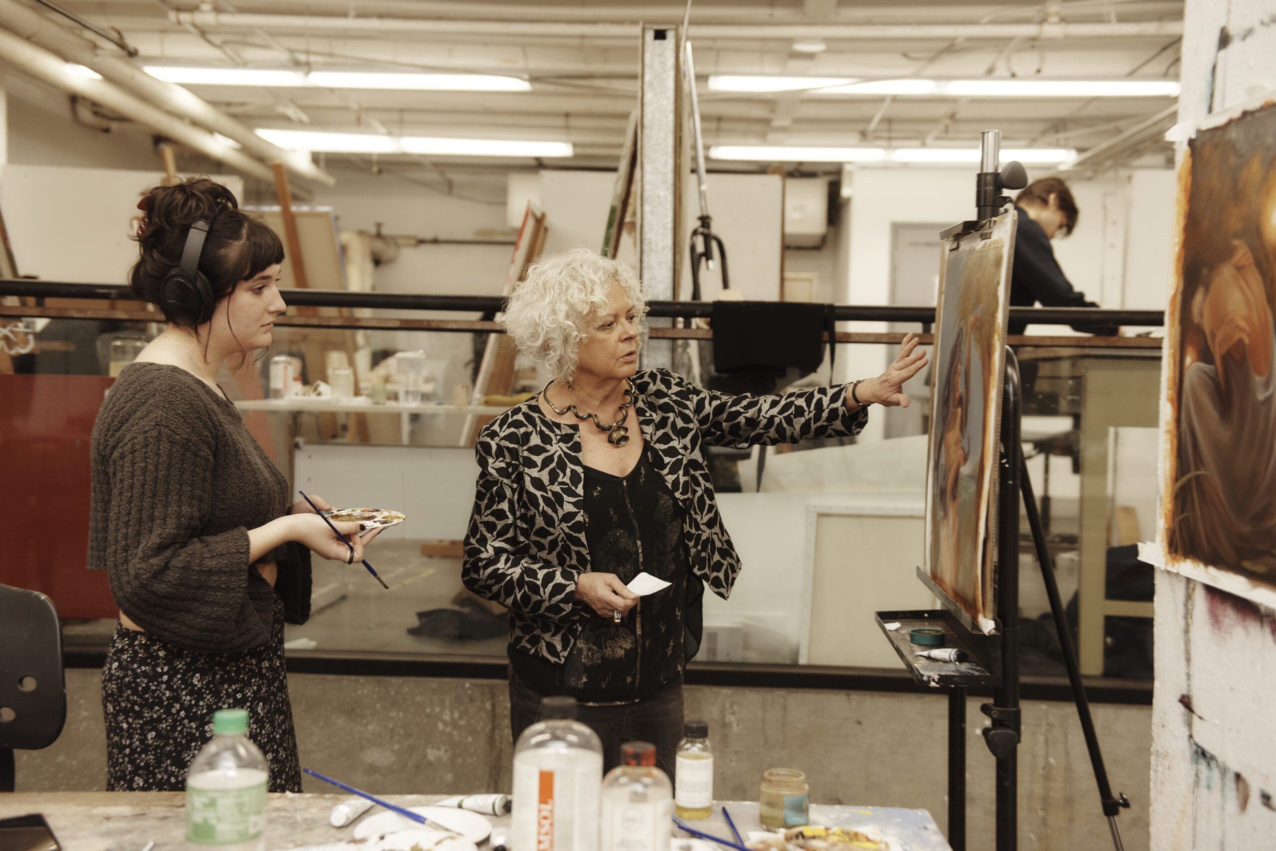 A faculty and student in a studio pointing to an artwork on a canvas.