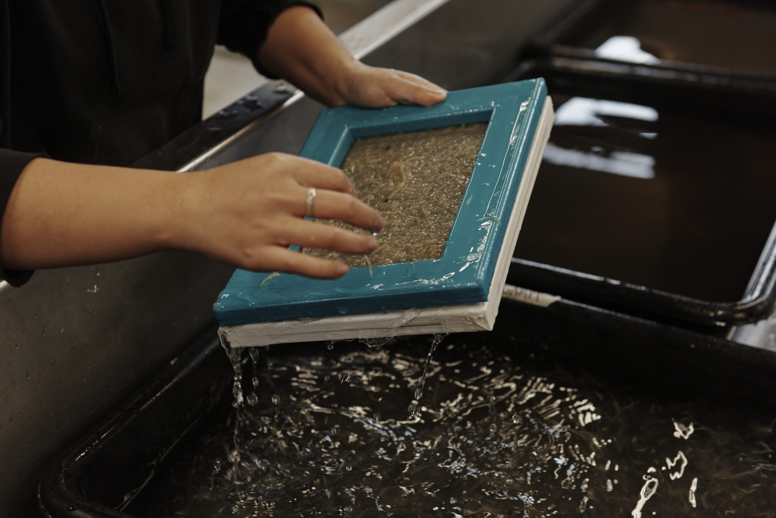 A hand holding a wet tray of paper pulp