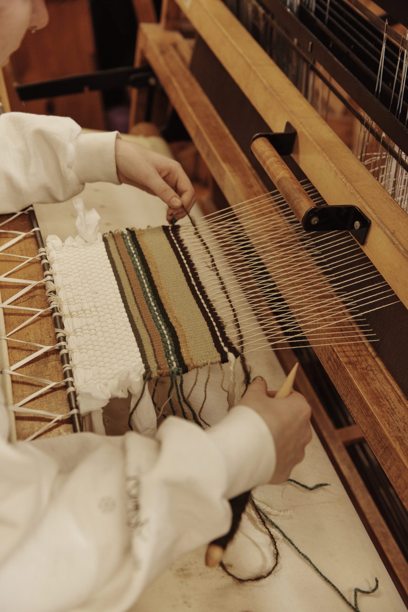 A student's hands weaving on a loom