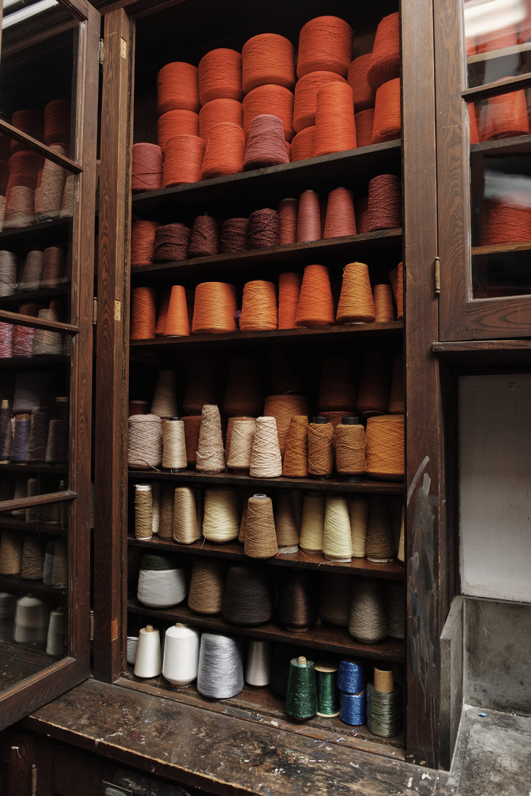 Red and orange yarn spools lined up neatly on shelves in a cabinet