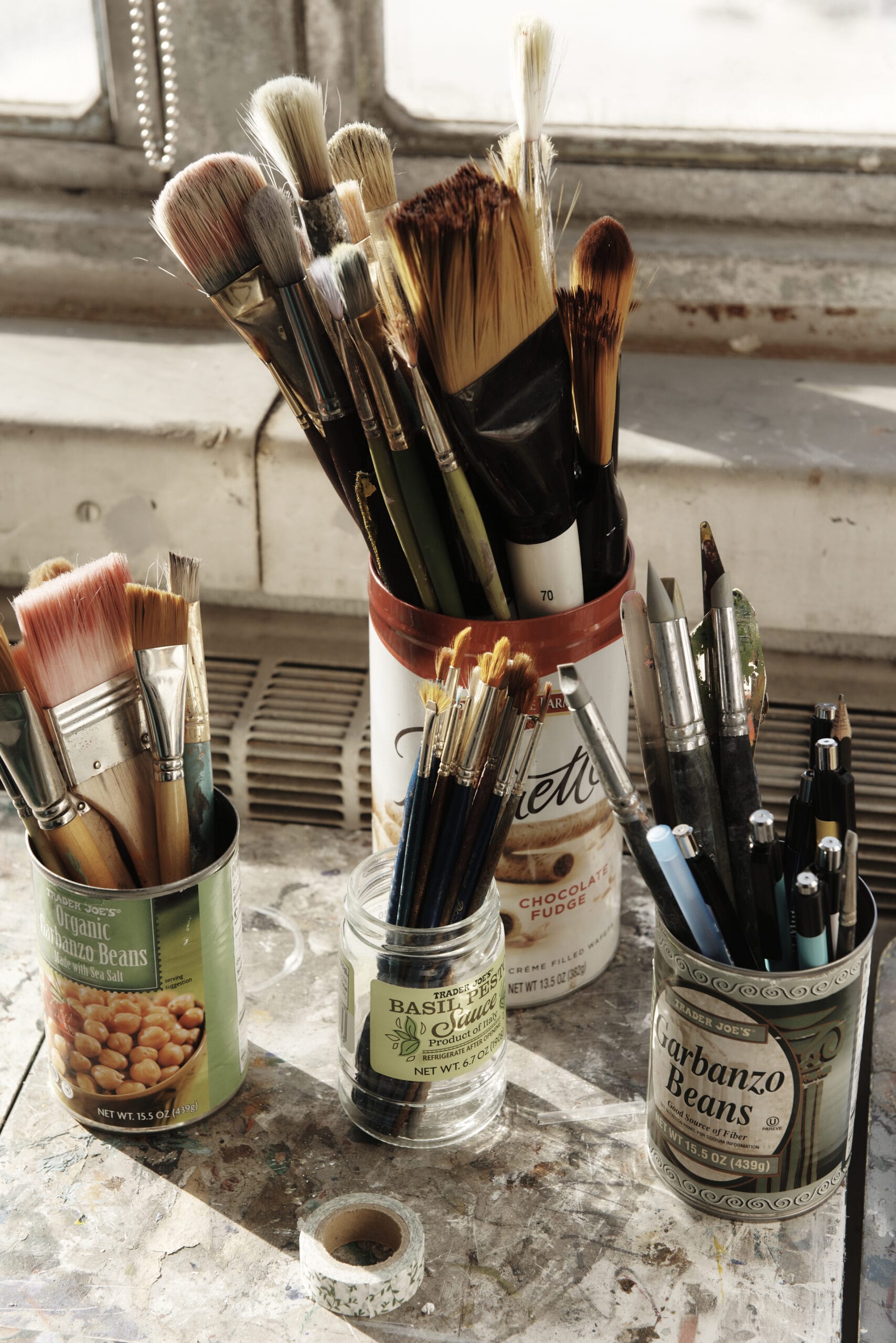 Cans of paint brushes on a table by the window.