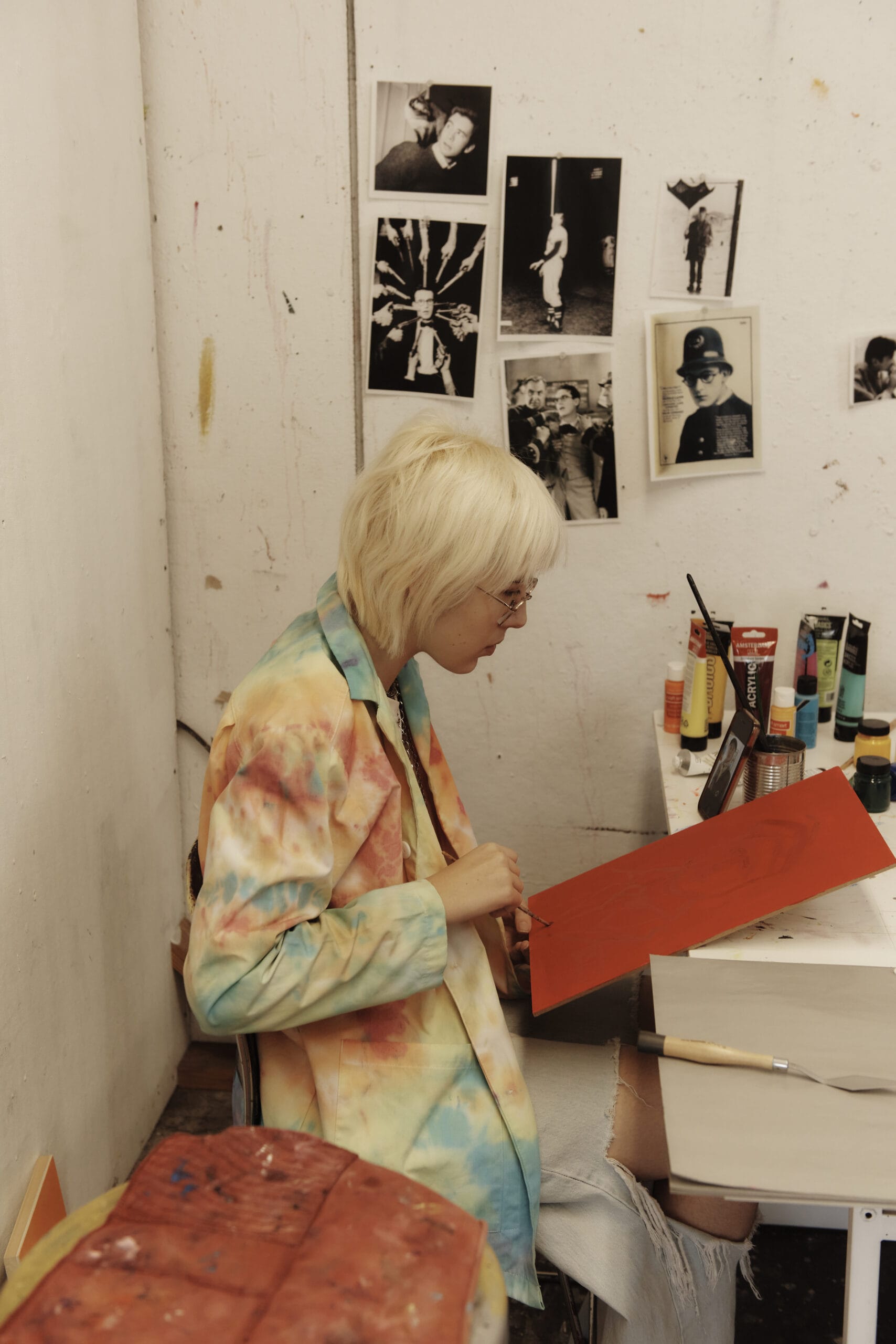 A woman sits at a red canvas, painting in her studio.