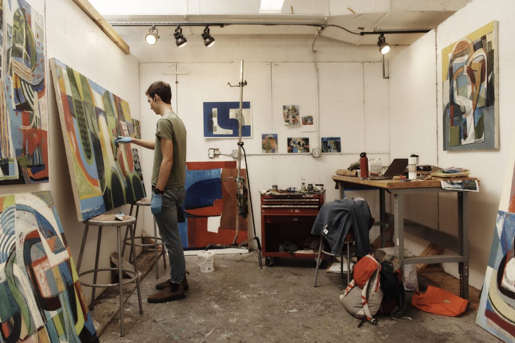 A student stands painting at a canvas in his studio.