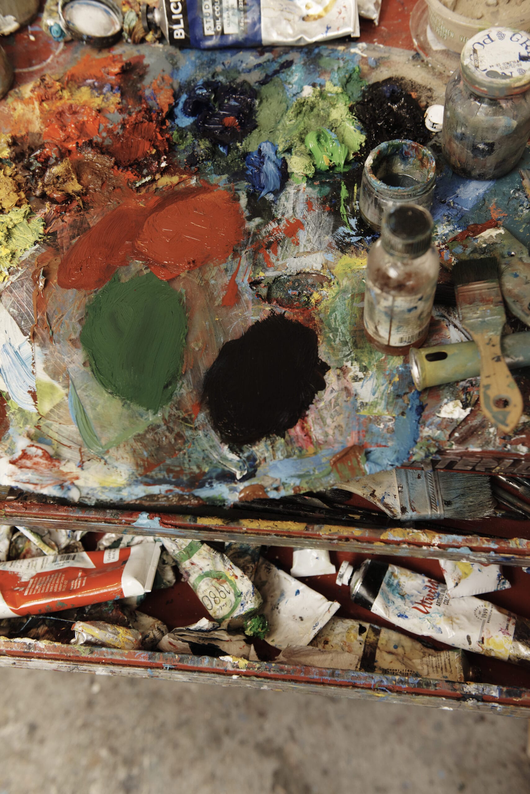 A colorful painting palette on a table, with a drawer of paint tubes