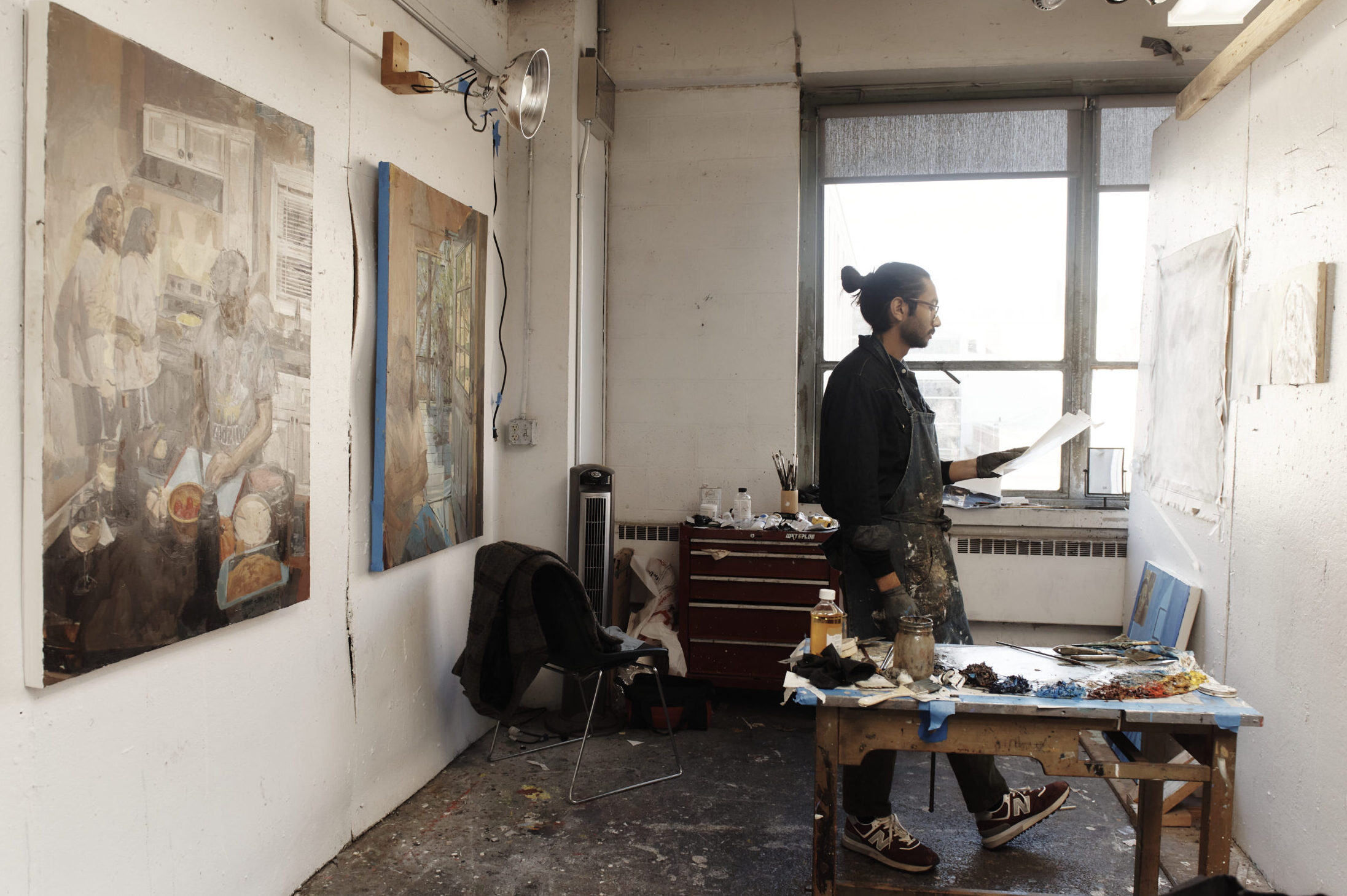 A backlit silhouette of a man, standing with a paintbrush in his hand, in his painting studio.