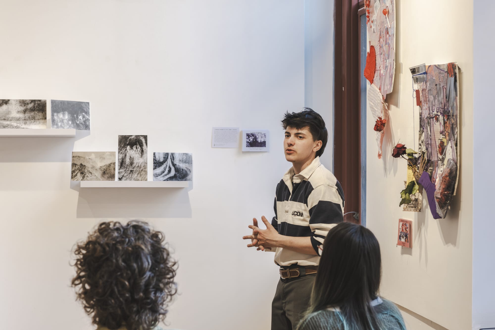A student stands in front of a wall of artwork, presenting to a group of people