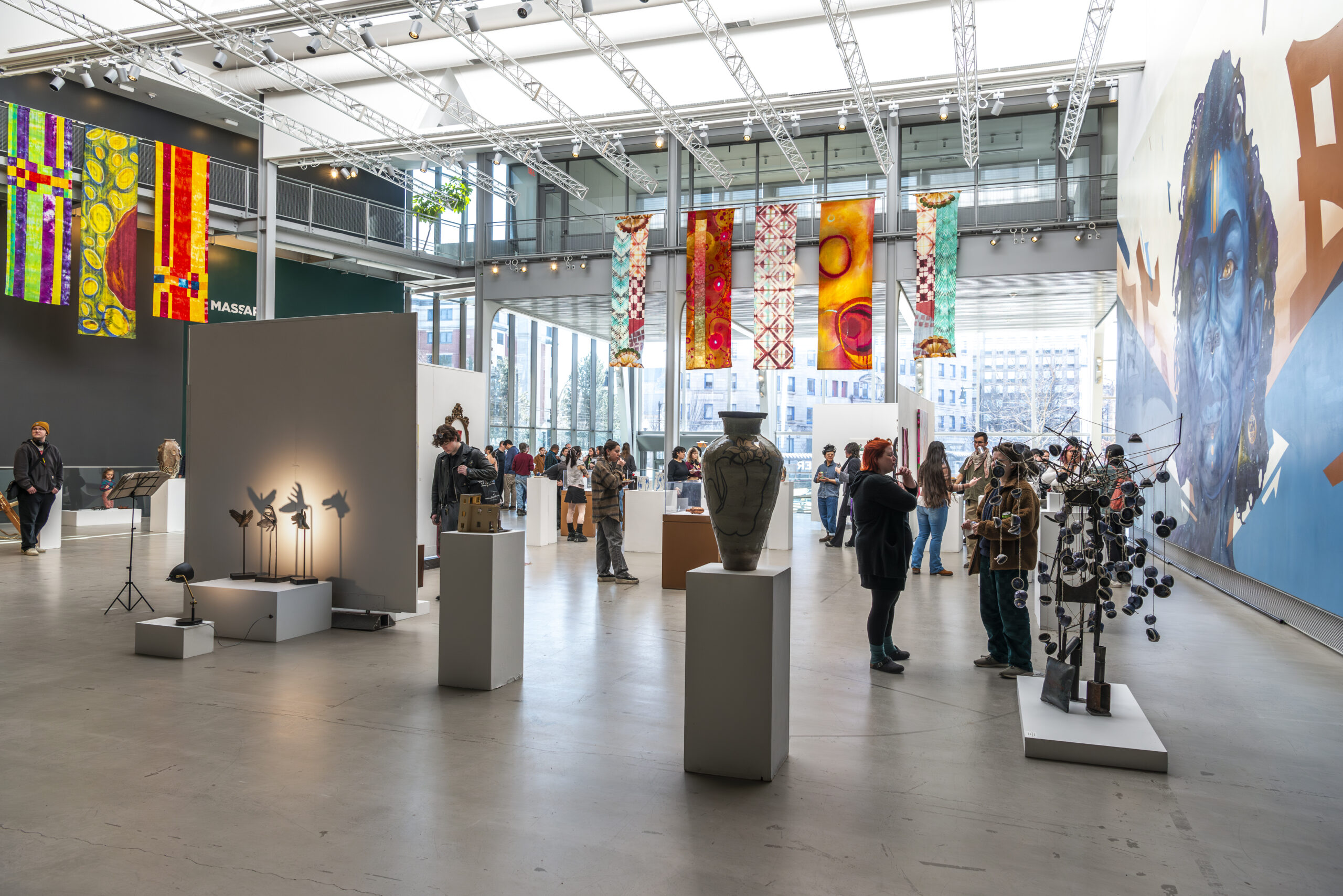 Exhibition guests observe 3 dimensional artwork on display in MassArt's Design and Media Center Atrium gallery.