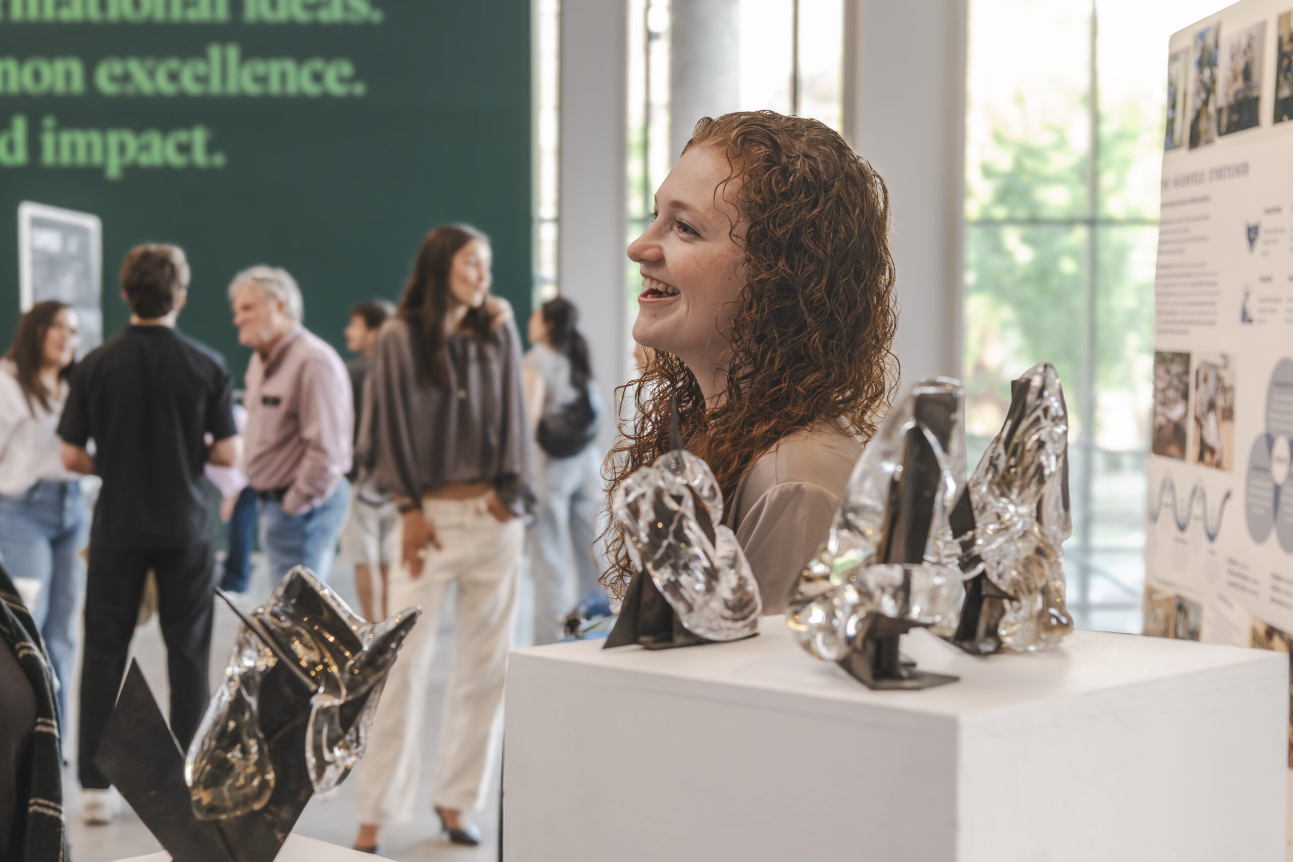 A student smiles at someone off camera in front of pedestals of glass work.