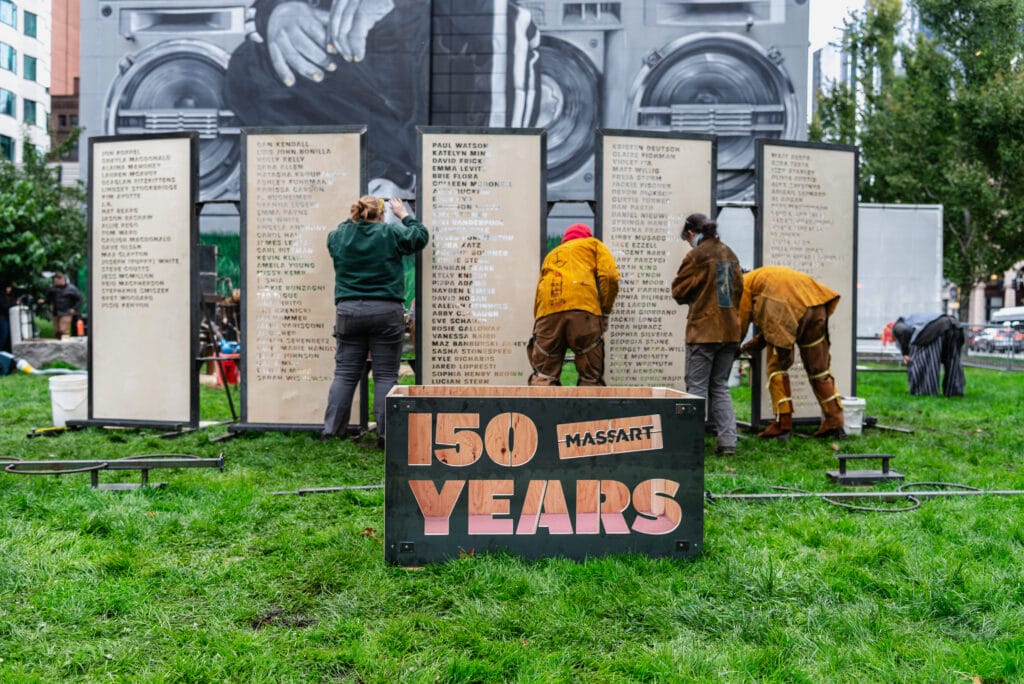 Students in the Iron Corps are setting up large panels of alumni names behind a large box that says "Massart 150 years."