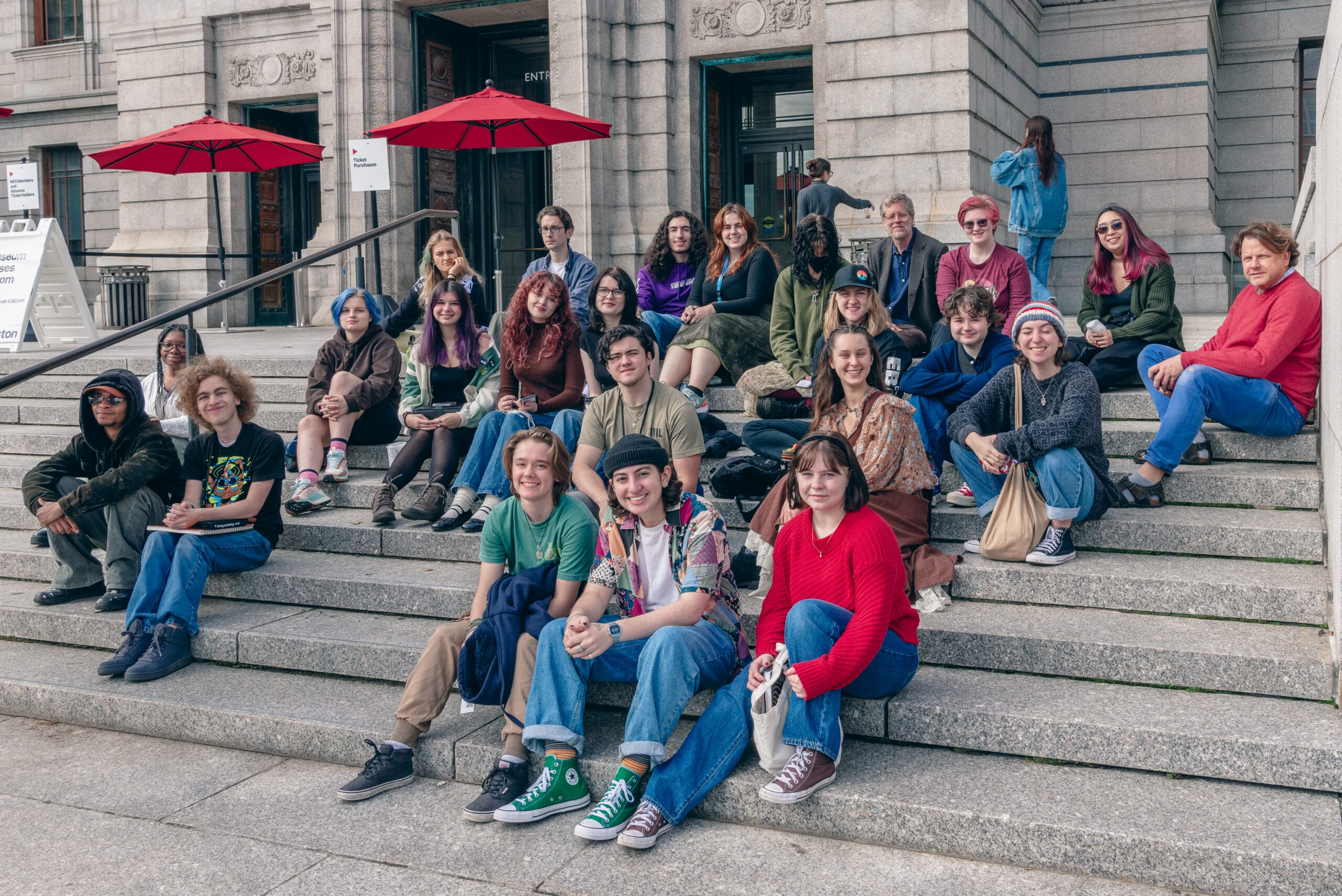 A large group of students sit on the steps of the Museum of Fine Arts in Boston.