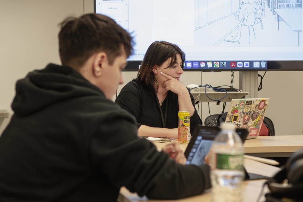 Two Graduate students sit looking at their laptops in an MFA Design classroom