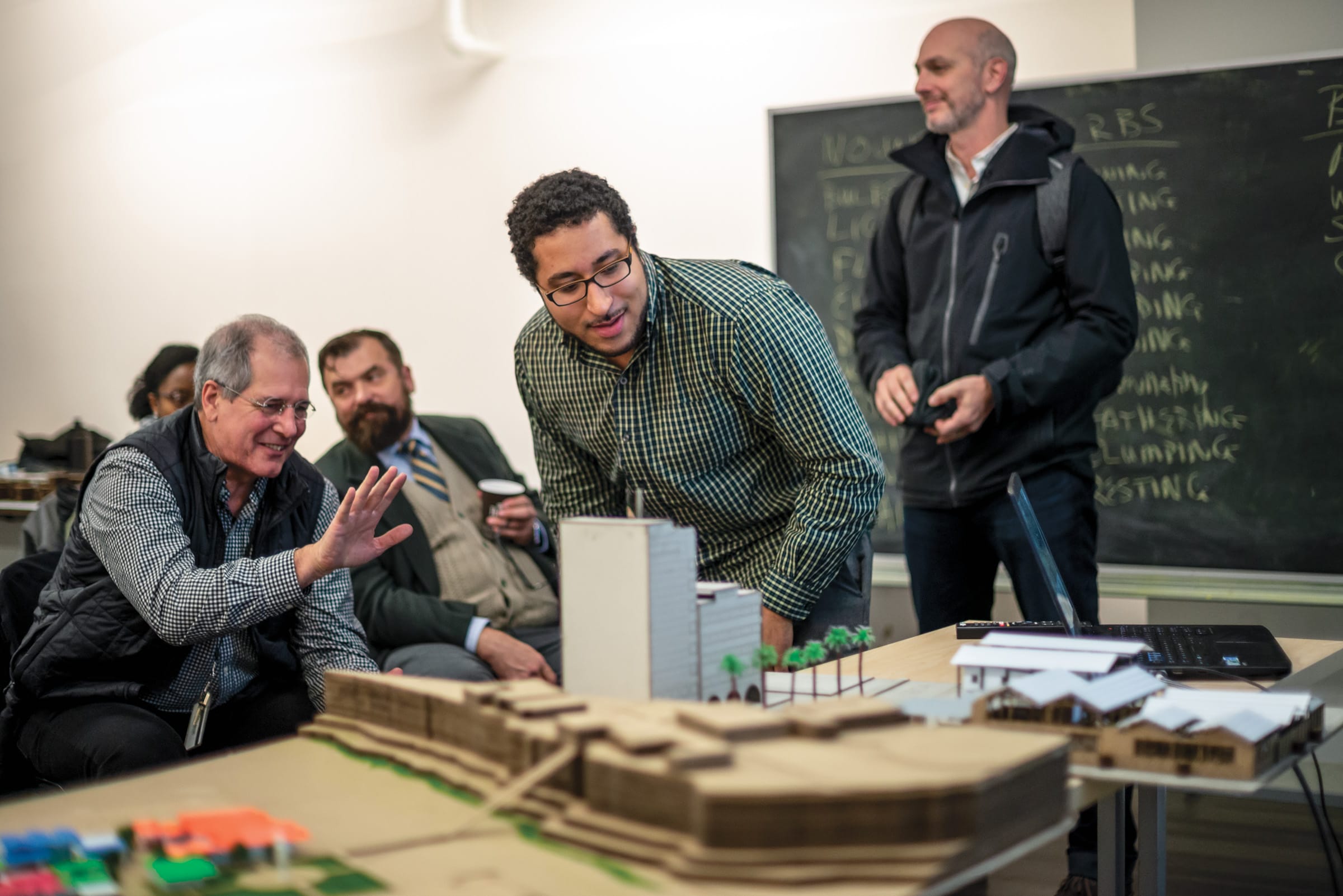 An architect gestures towards an architectural model while speaking to a student.