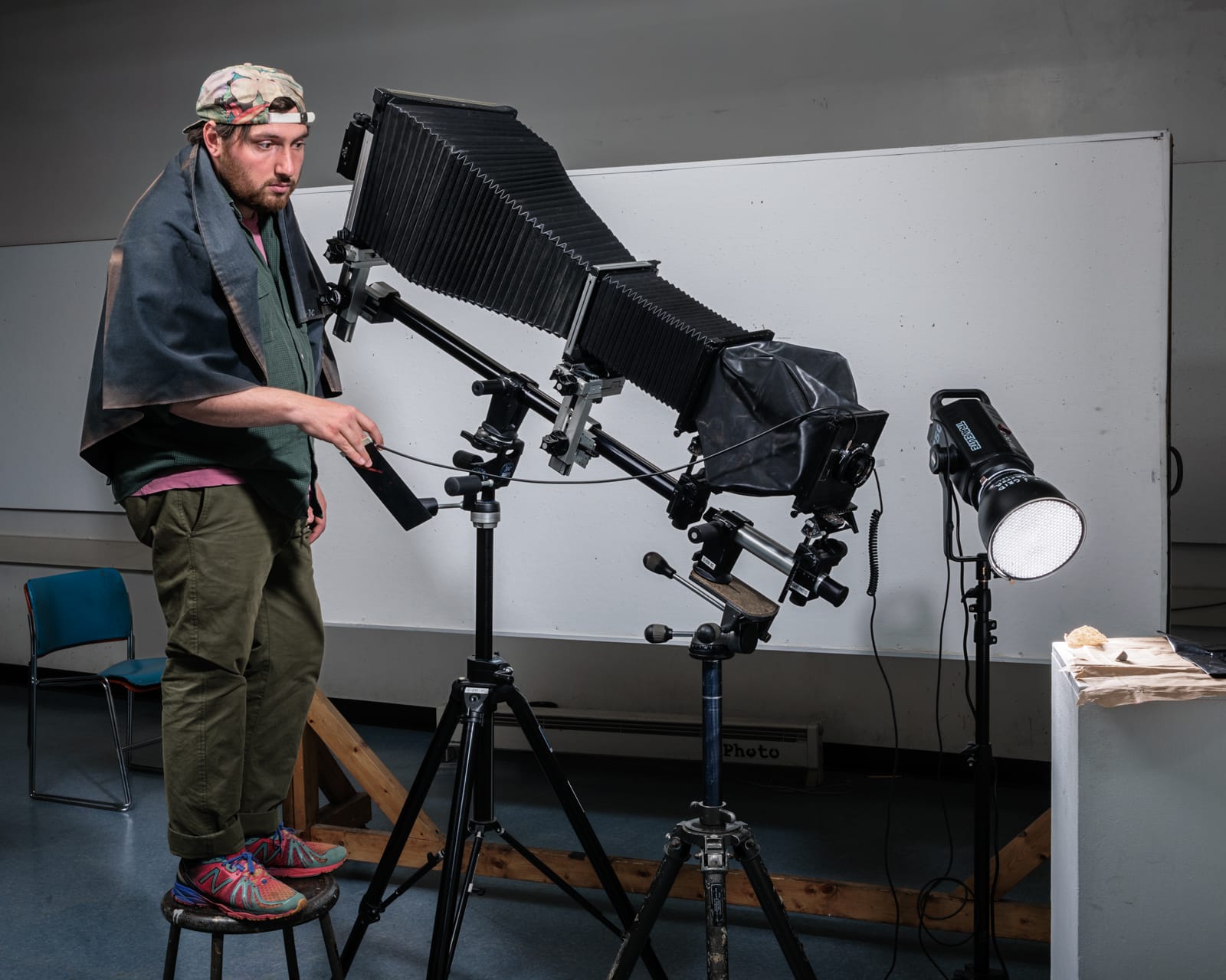 A man with an MFA Photography background stands next to a large camera, exemplifying his expertise and passion for the art.