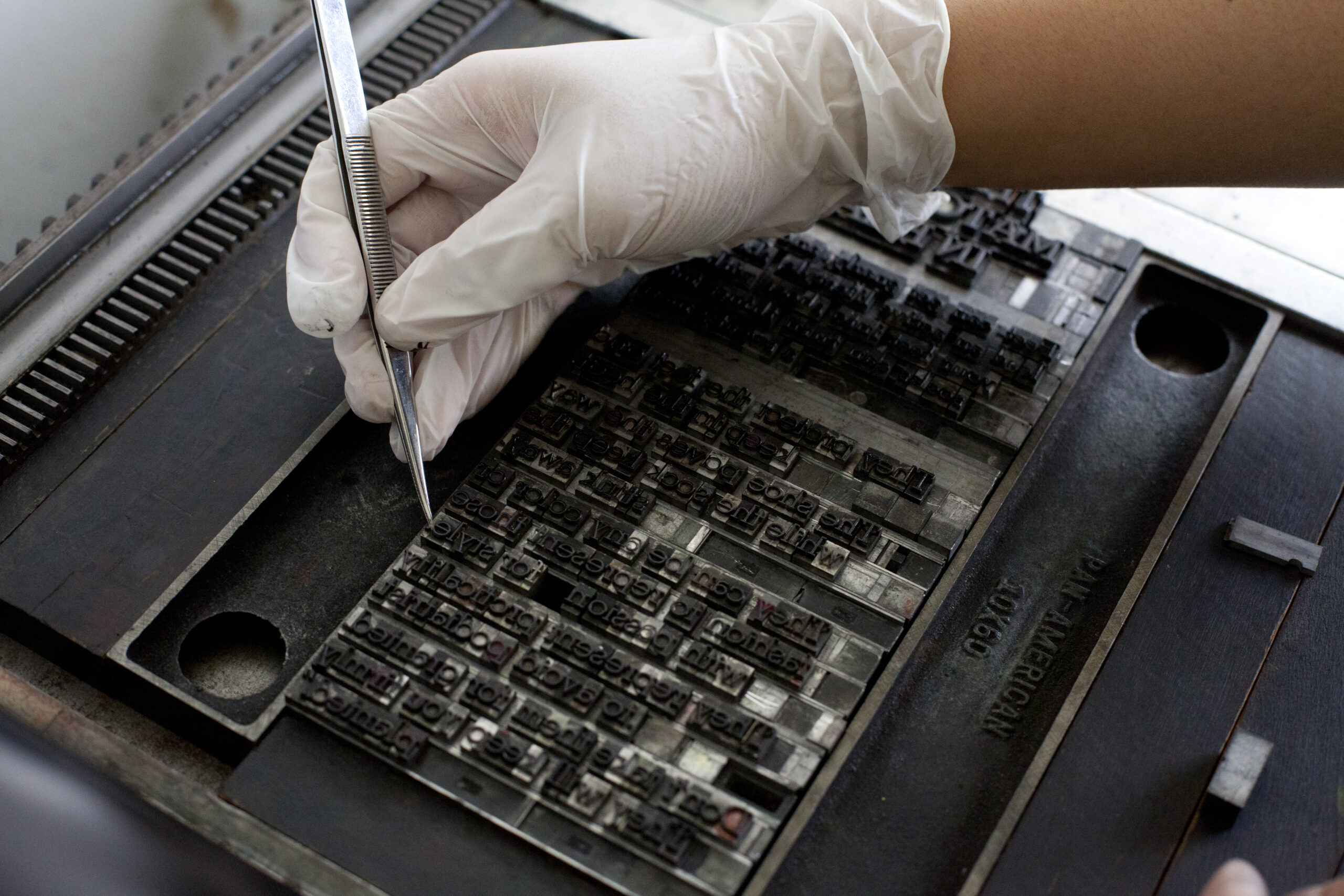 A hand picking up letterpress type with tweezers.