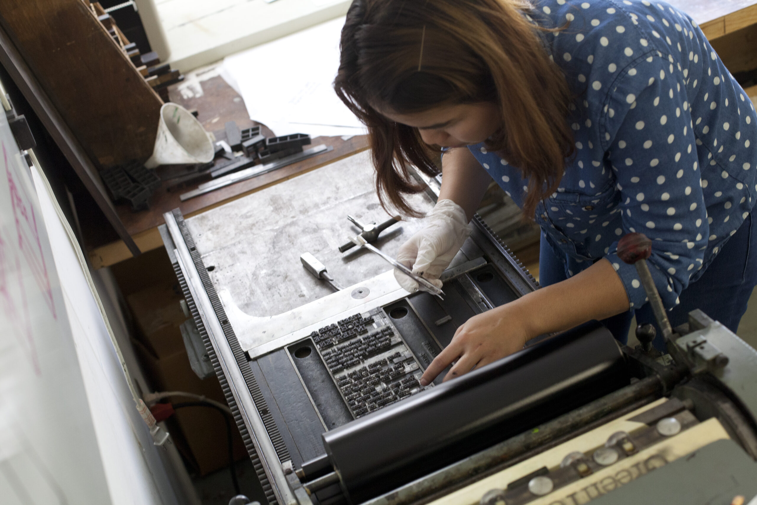 Student bent over a Letterpress, lining up block type.