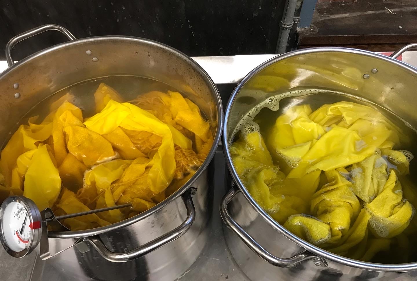 Two pots of yellow and orange dye with fabric submerged under water.