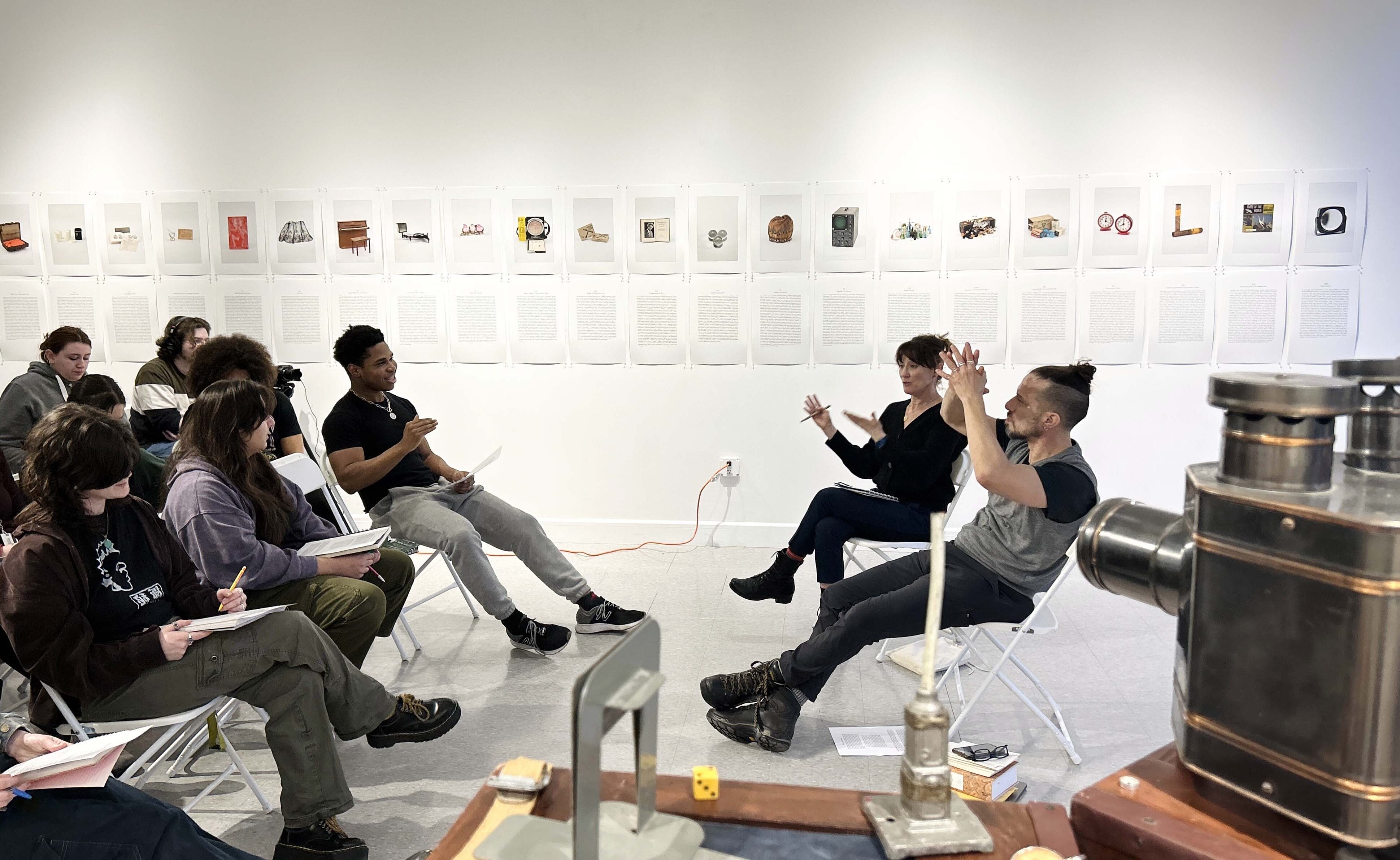 A group listens and takes notes as two people speak in front of artwork at Brant Gallery.