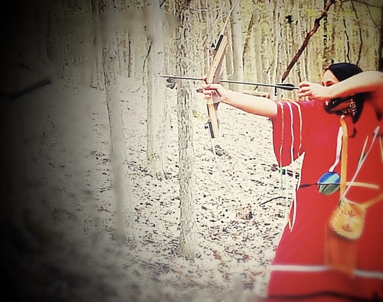 Image of a woman dressed in red aiming a bow & arrow.