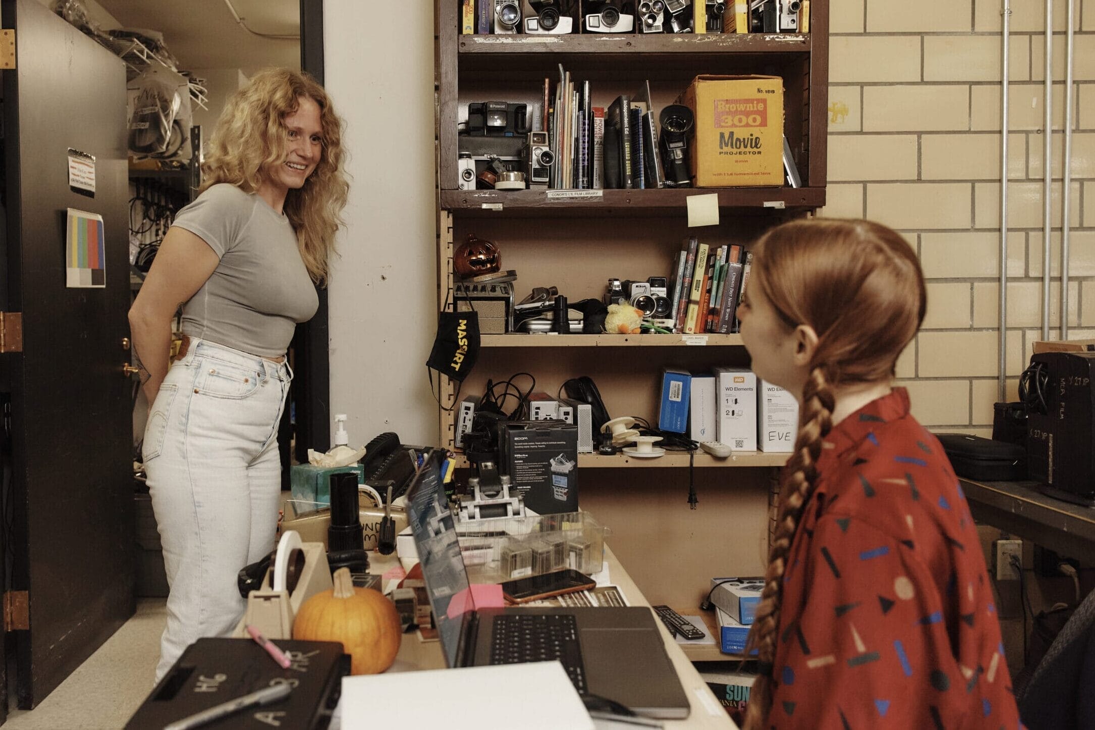 A woman stands in a doorway smiling a a student seated behind a desk.