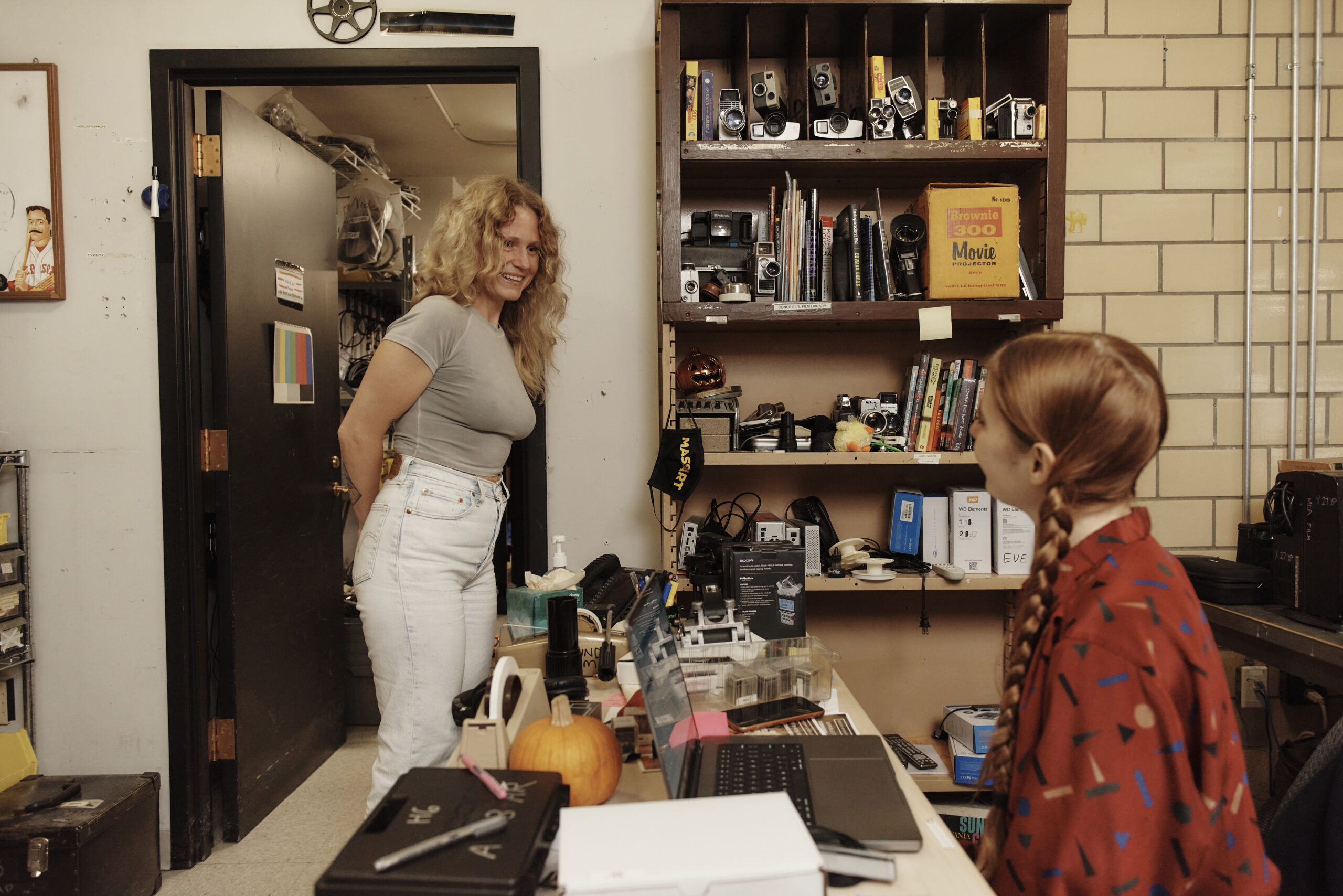 A woman stands in a doorway smiling a a student seated behind a desk.